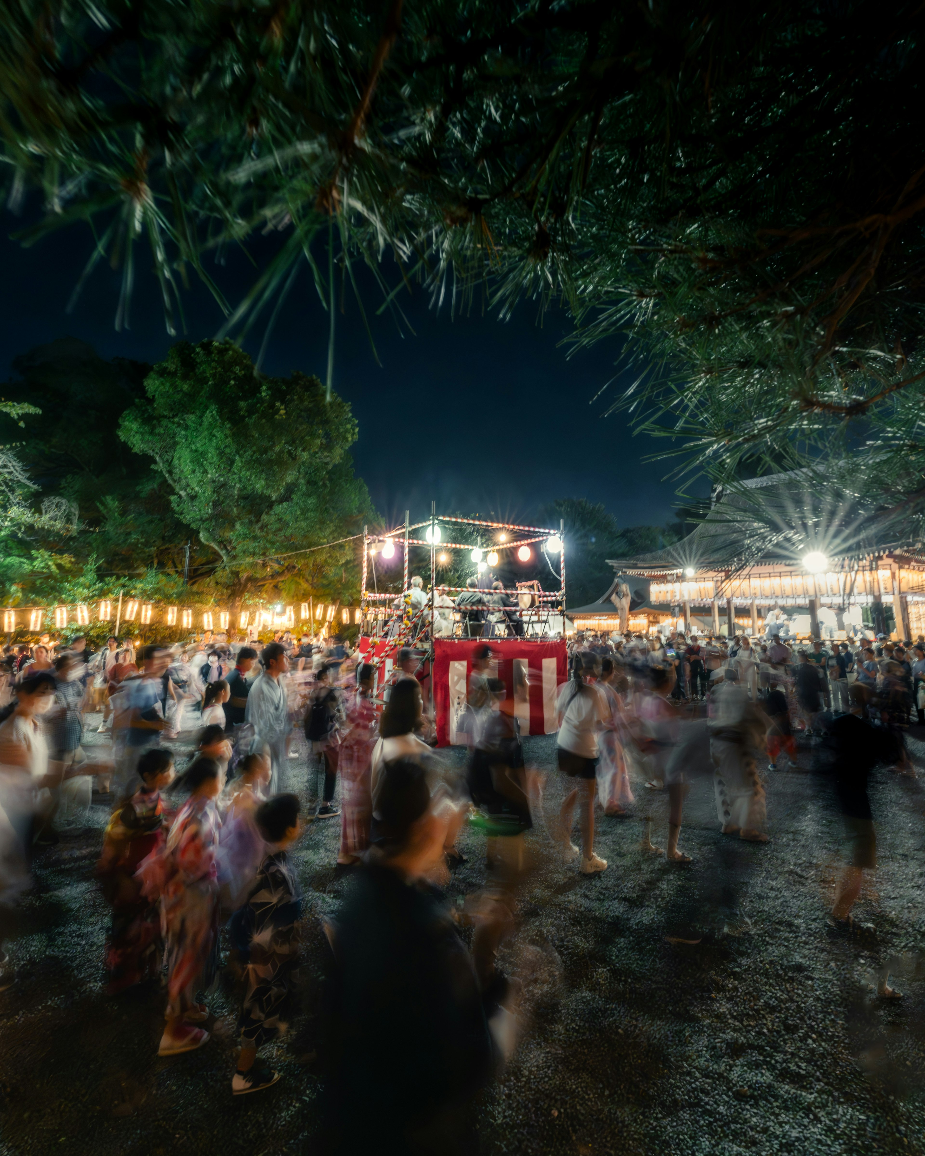 Orang-orang menari di festival malam dengan stan makanan dan lampu