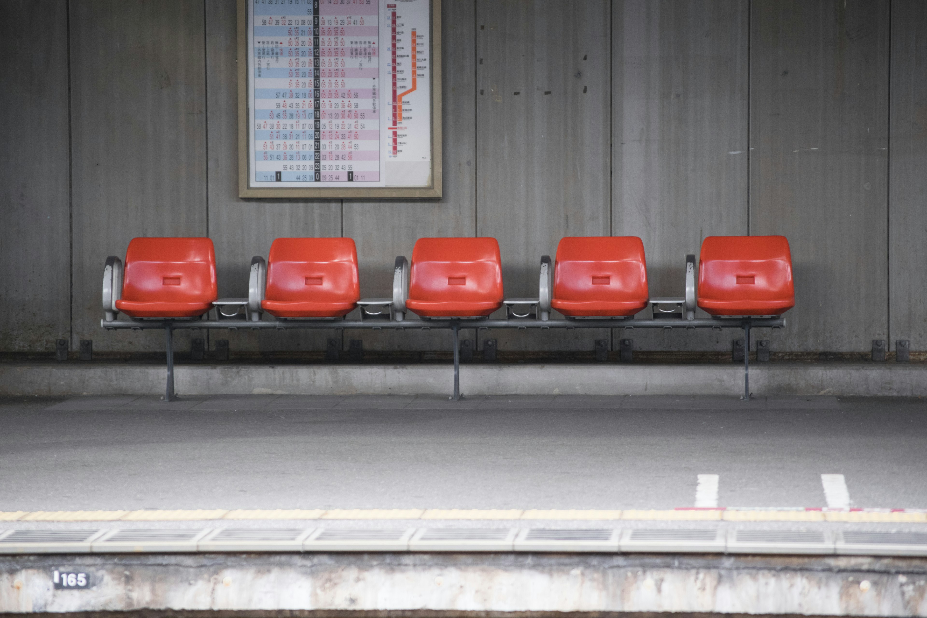 Reihe roter Stühle auf einem Bahnhofsperron