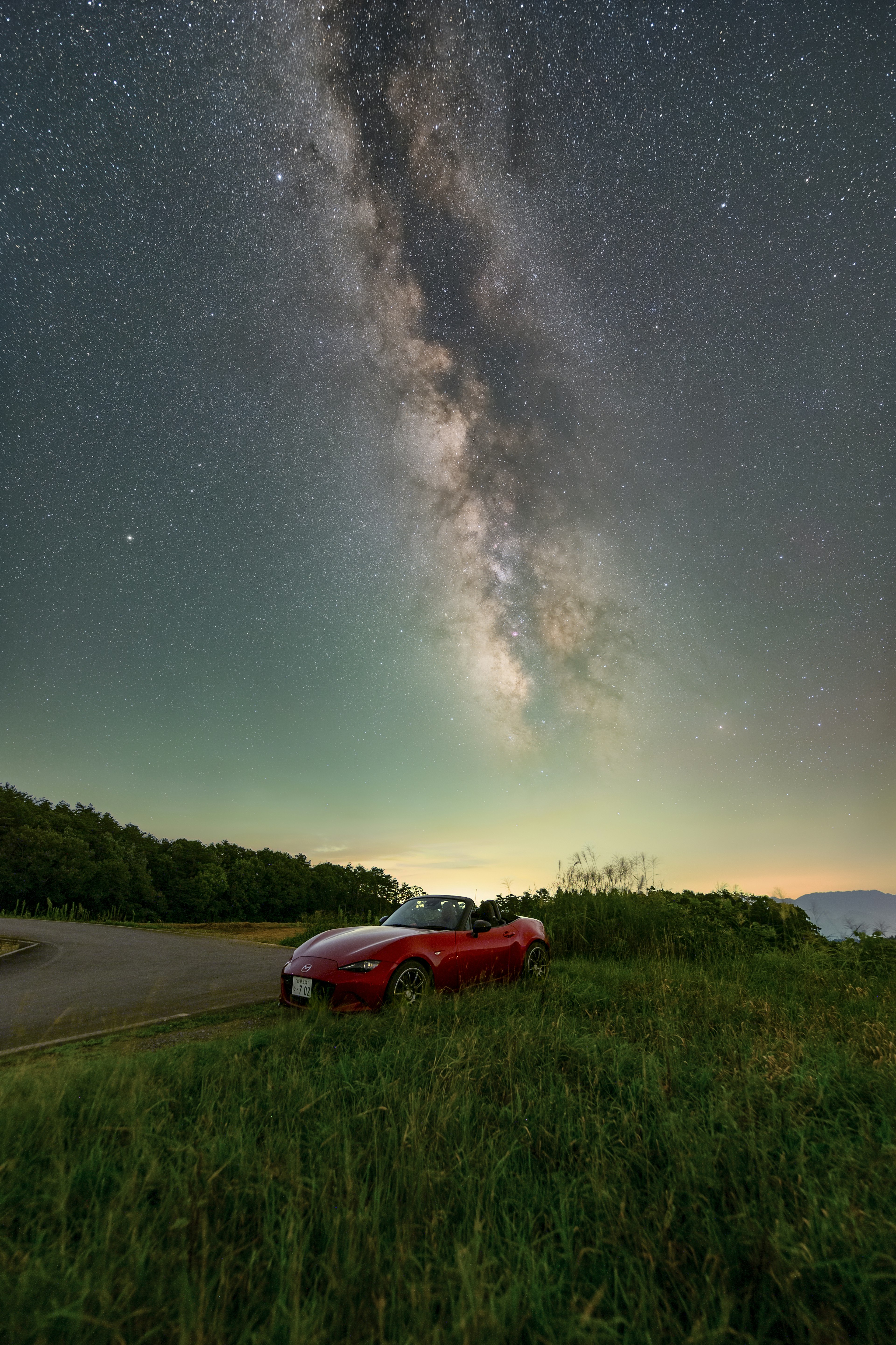 Ein rotes Auto, das in einem bewachsenen Bereich unter einem beeindruckenden Sternenhimmel parkt