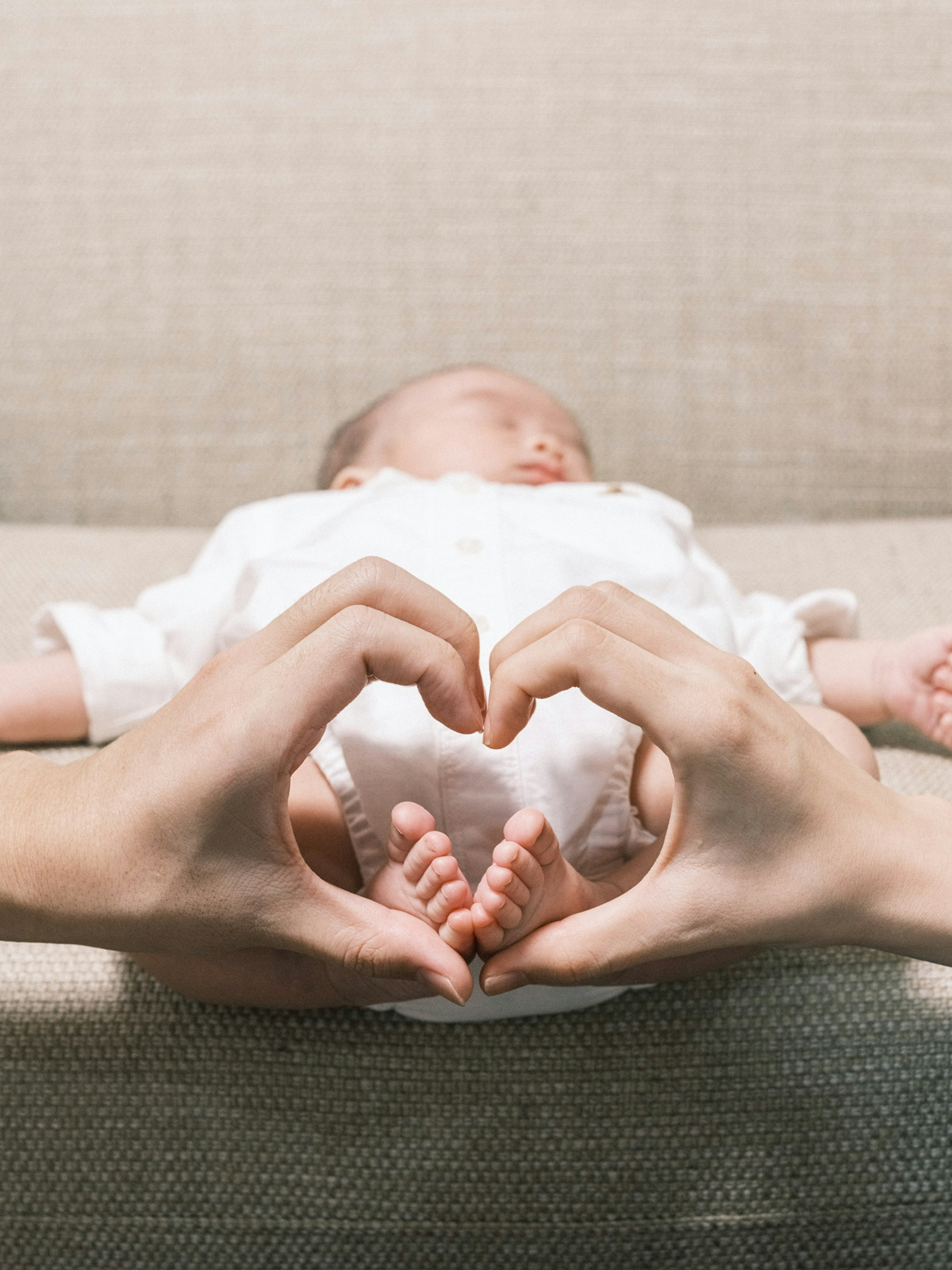 Hands forming a heart shape around a sleeping baby with tiny feet