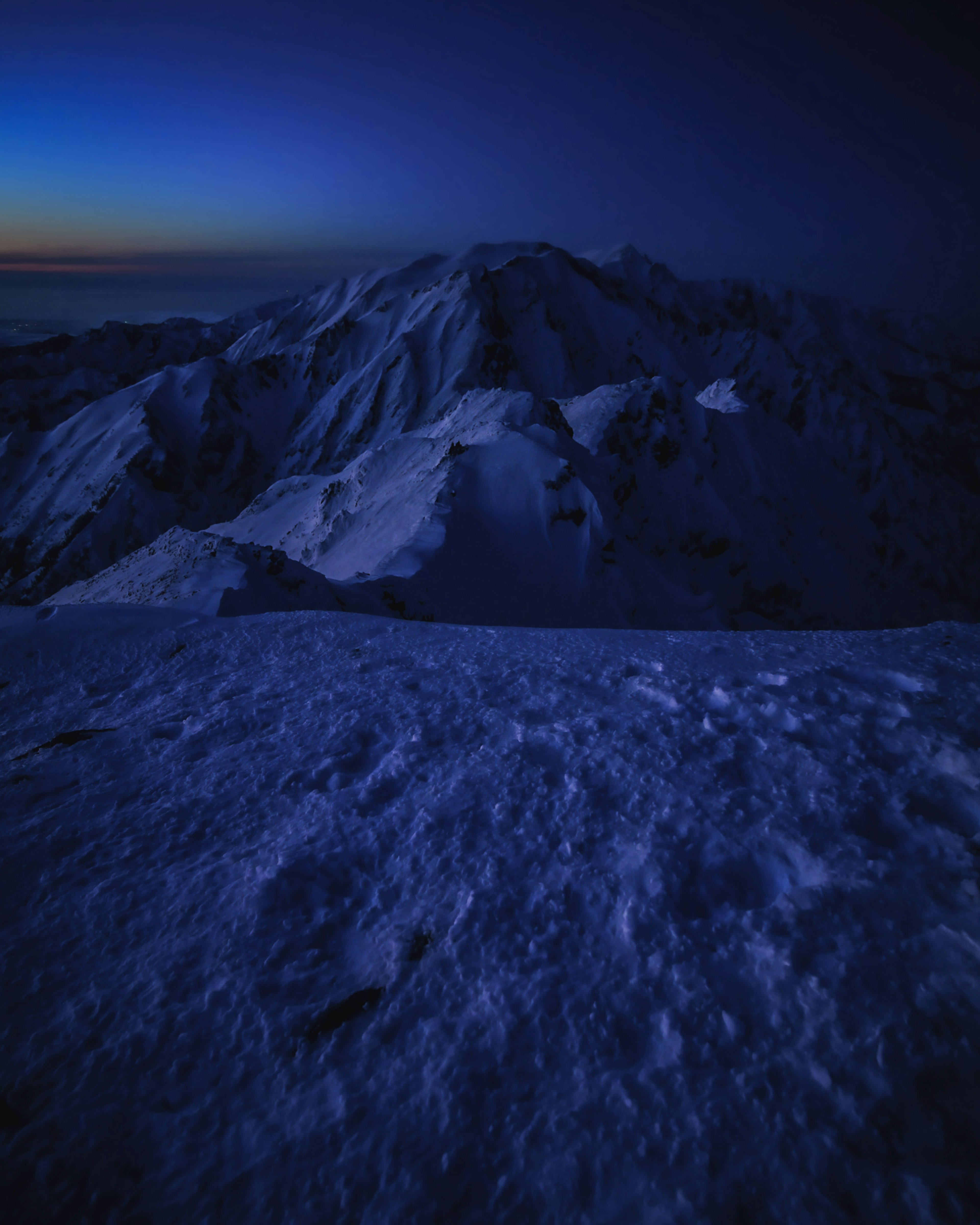 Schneebedeckte Berge, die im Dämmerlicht in blauen Farbtönen leuchten