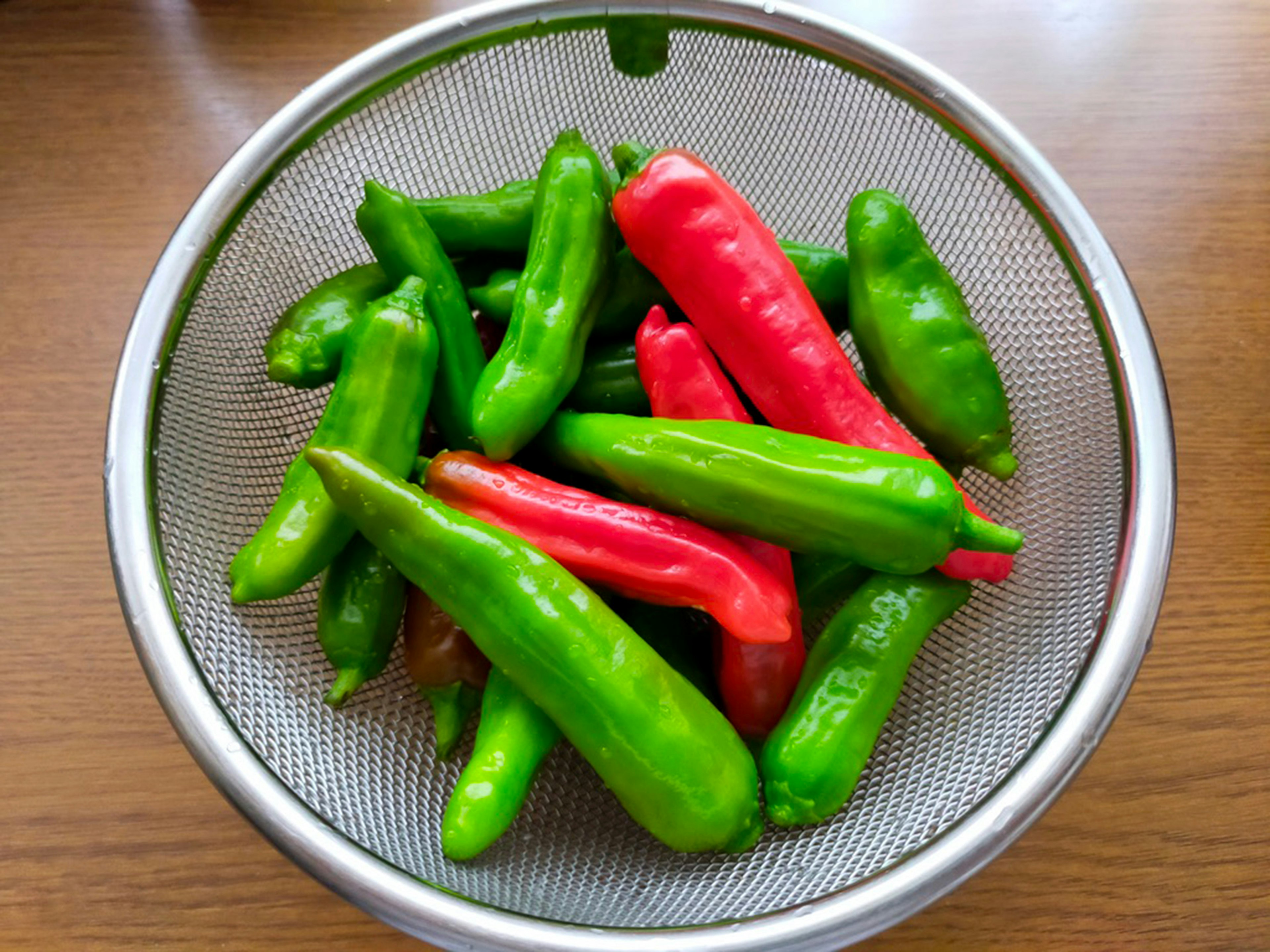 Fresh green and red chilies in a strainer on a wooden surface