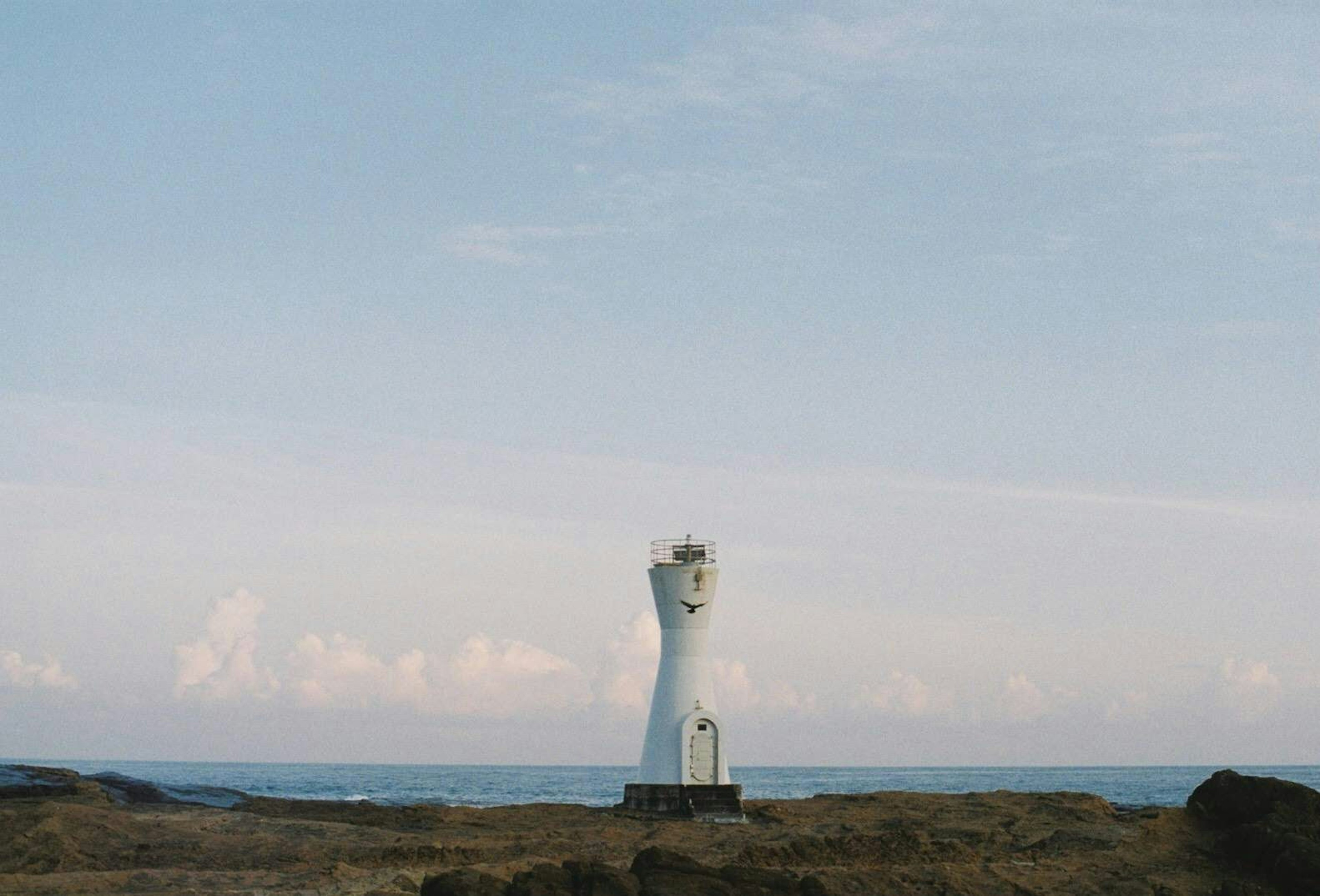 A white lighthouse standing near the sea with a clear sky