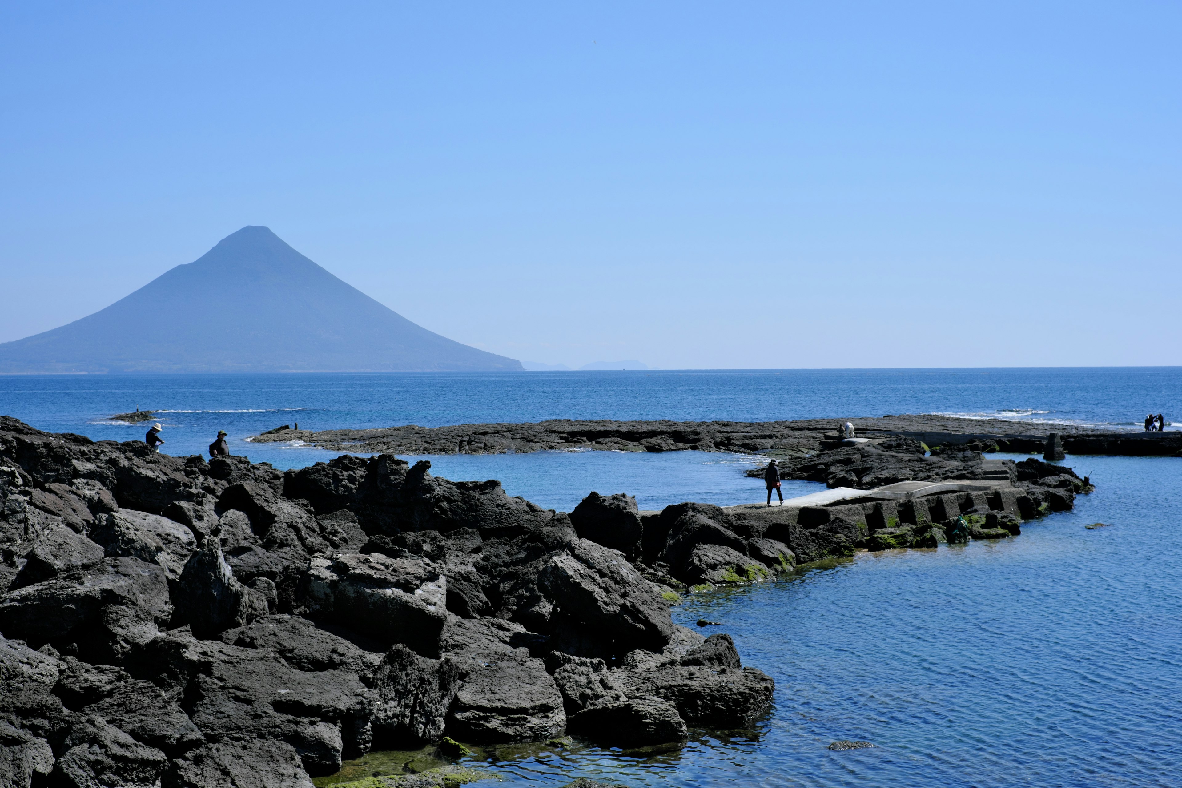 Vista escénica de un volcán y el océano bajo un cielo azul claro con costa rocosa