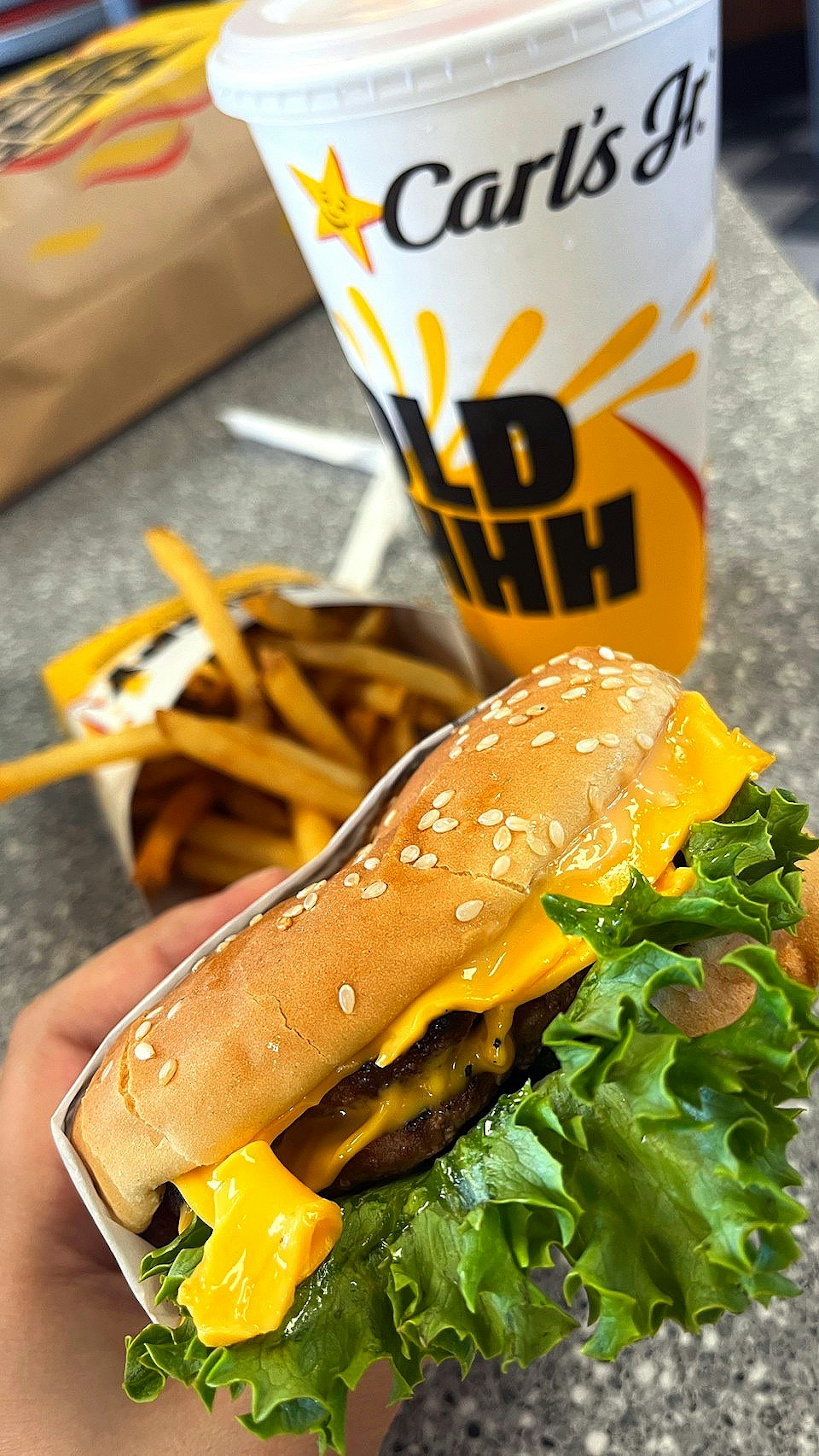 Hamburger Carl's Jr con lattuga e formaggio insieme a patatine e una bevanda