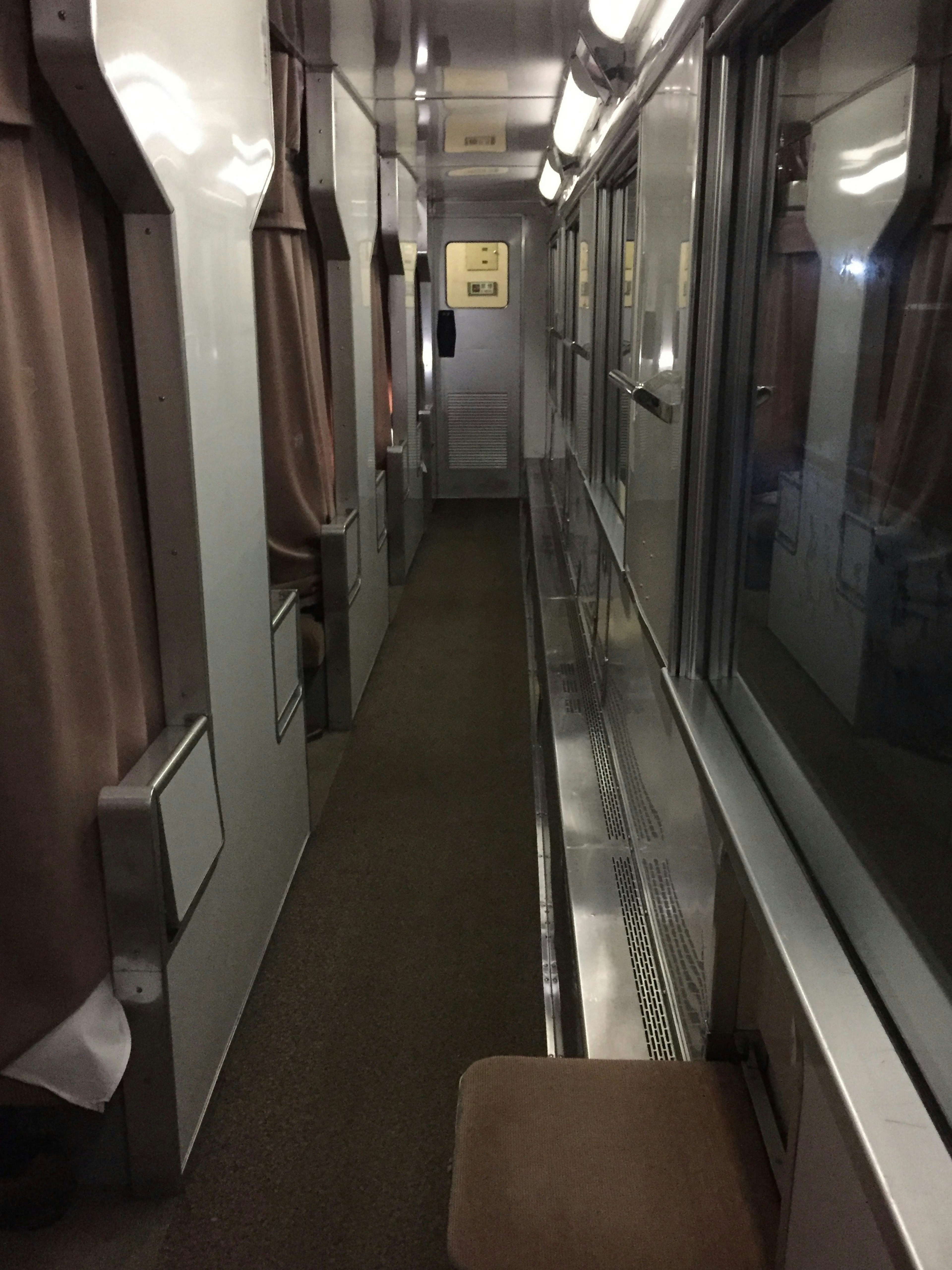 Pasillo interior de un vagón de tren con cortinas en las ventanas y una mesa de metal al lado de un asiento