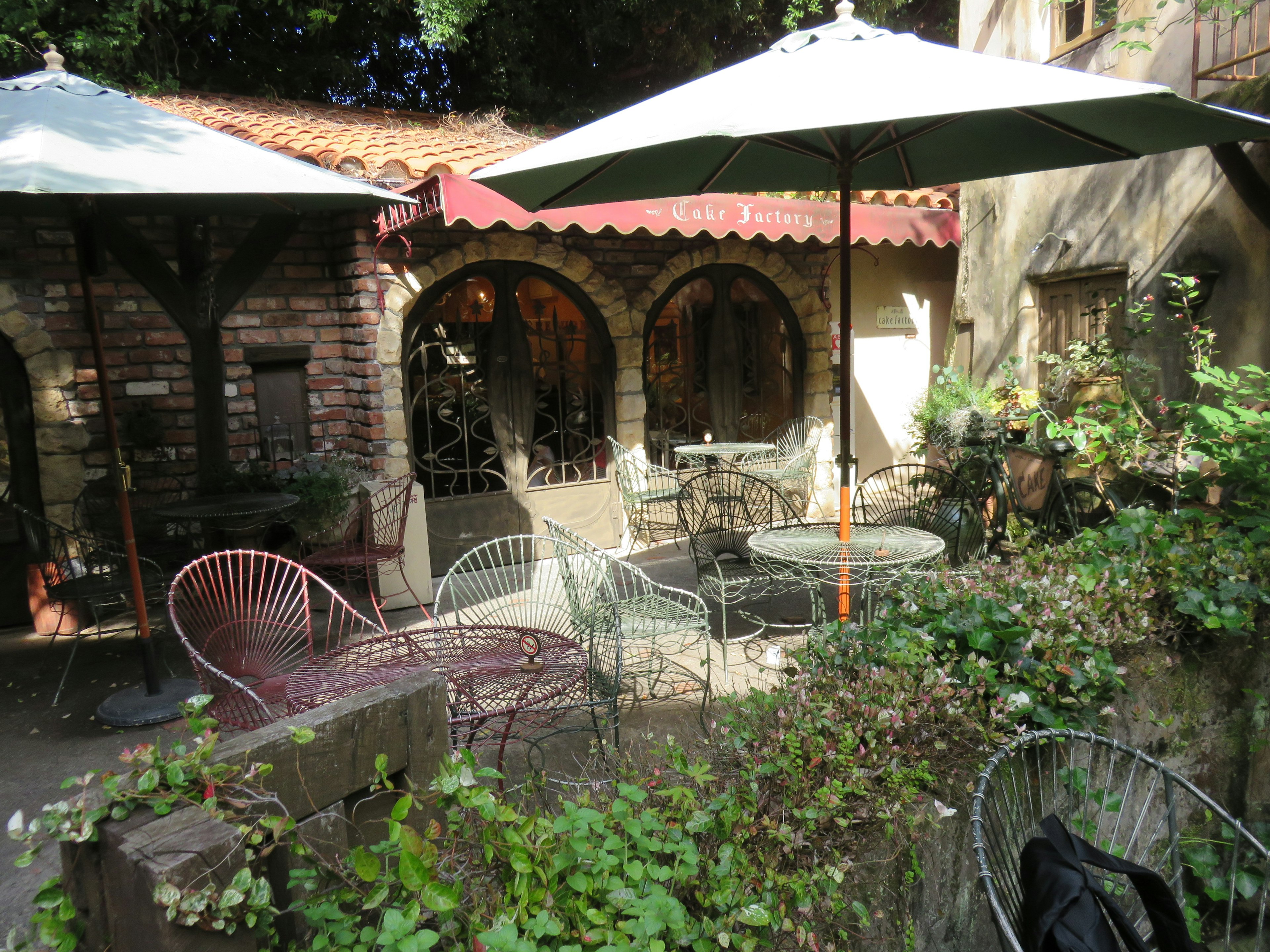 Terrasse de café pittoresque entourée de verdure avec des chaises et tables en fer forgé sous des parasols