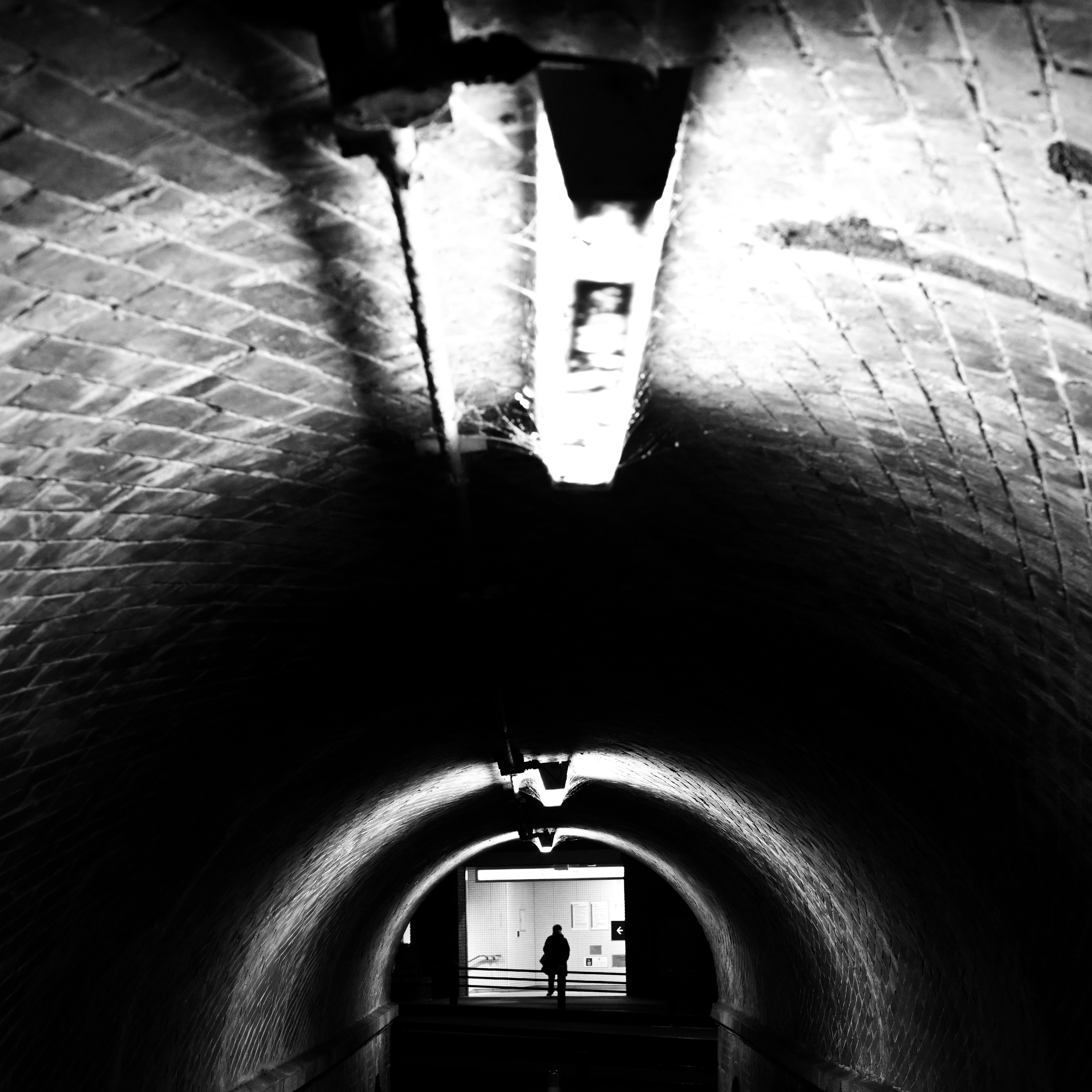 A silhouette of a person standing at the end of a dark tunnel with bright exit