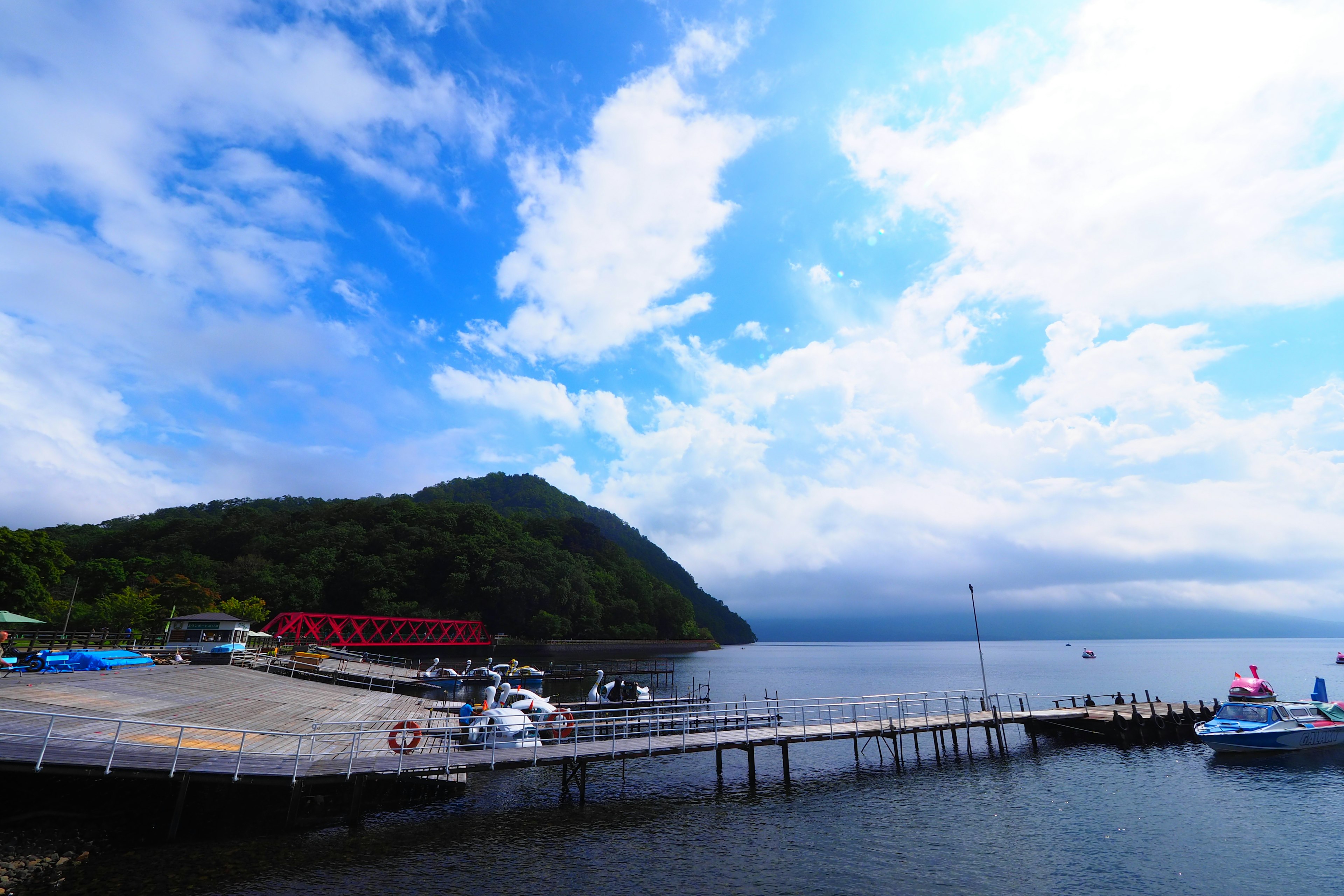 Coastal landscape with blue sky and clouds docked boats at a pier and green hill