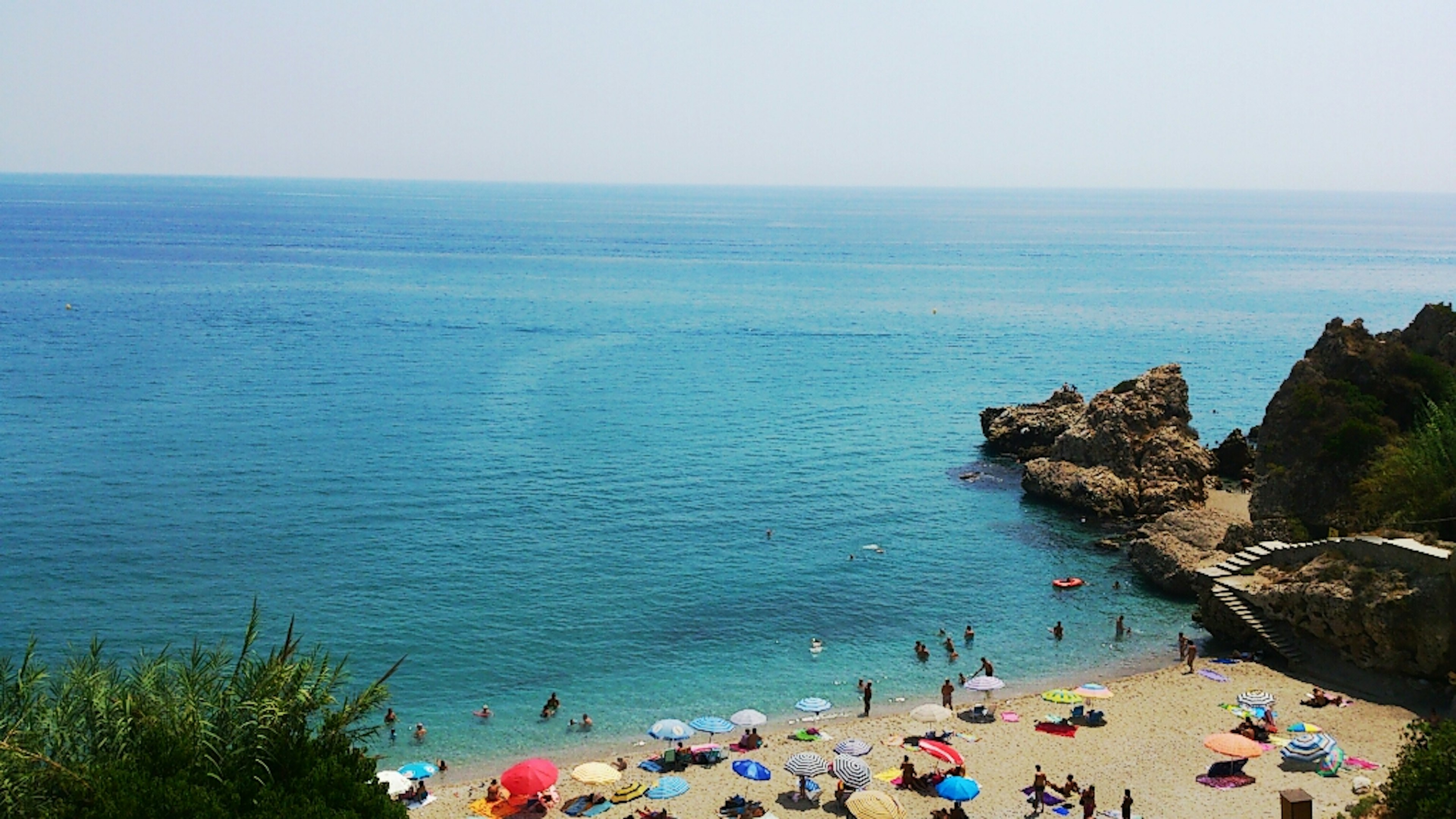 Malersicher Blick auf einen Strand mit blauem Wasser und bunten Sonnenschirmen