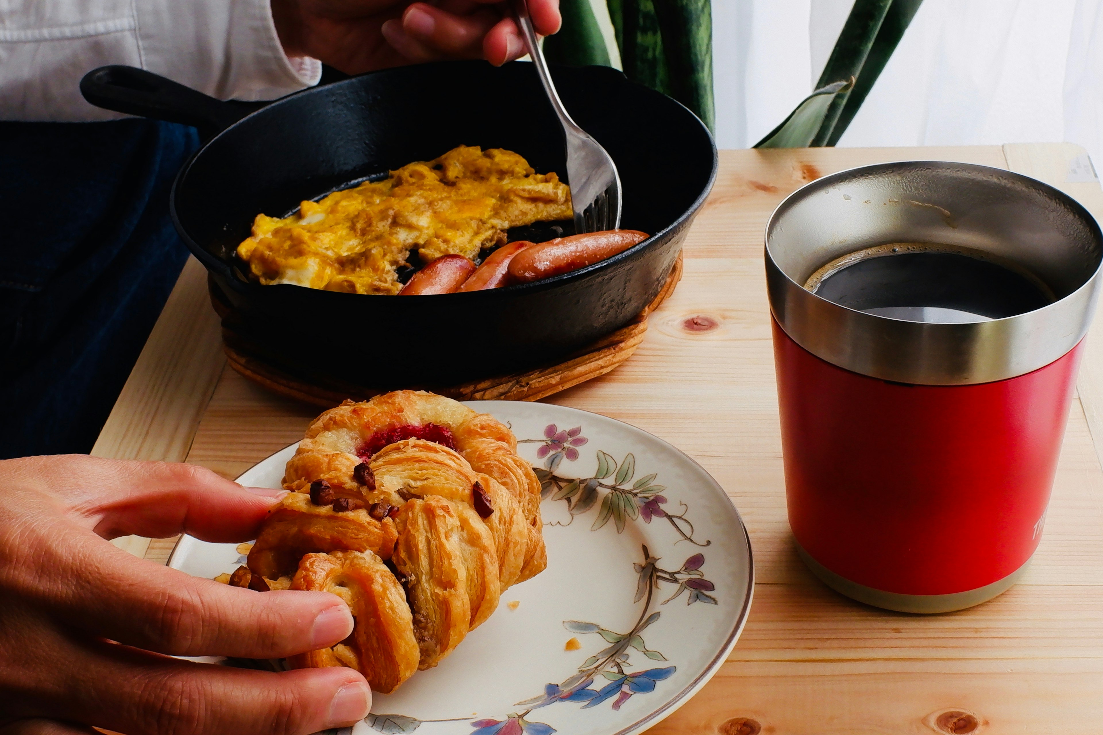 朝食のプレートに卵料理とソーセージを盛ったスキレットとカフェに手を伸ばす