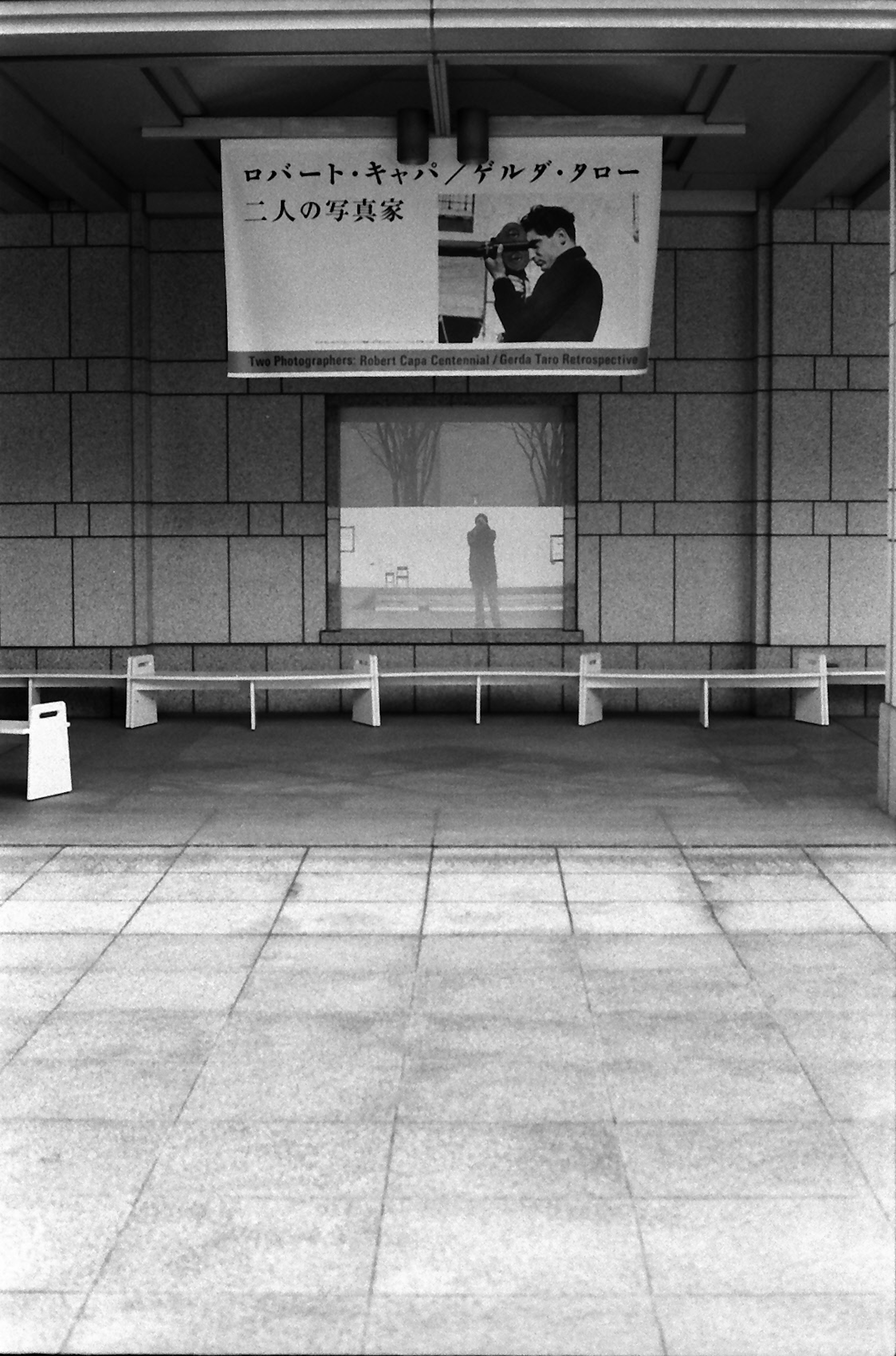 Black and white photo of an empty train station waiting area with a person's shadow