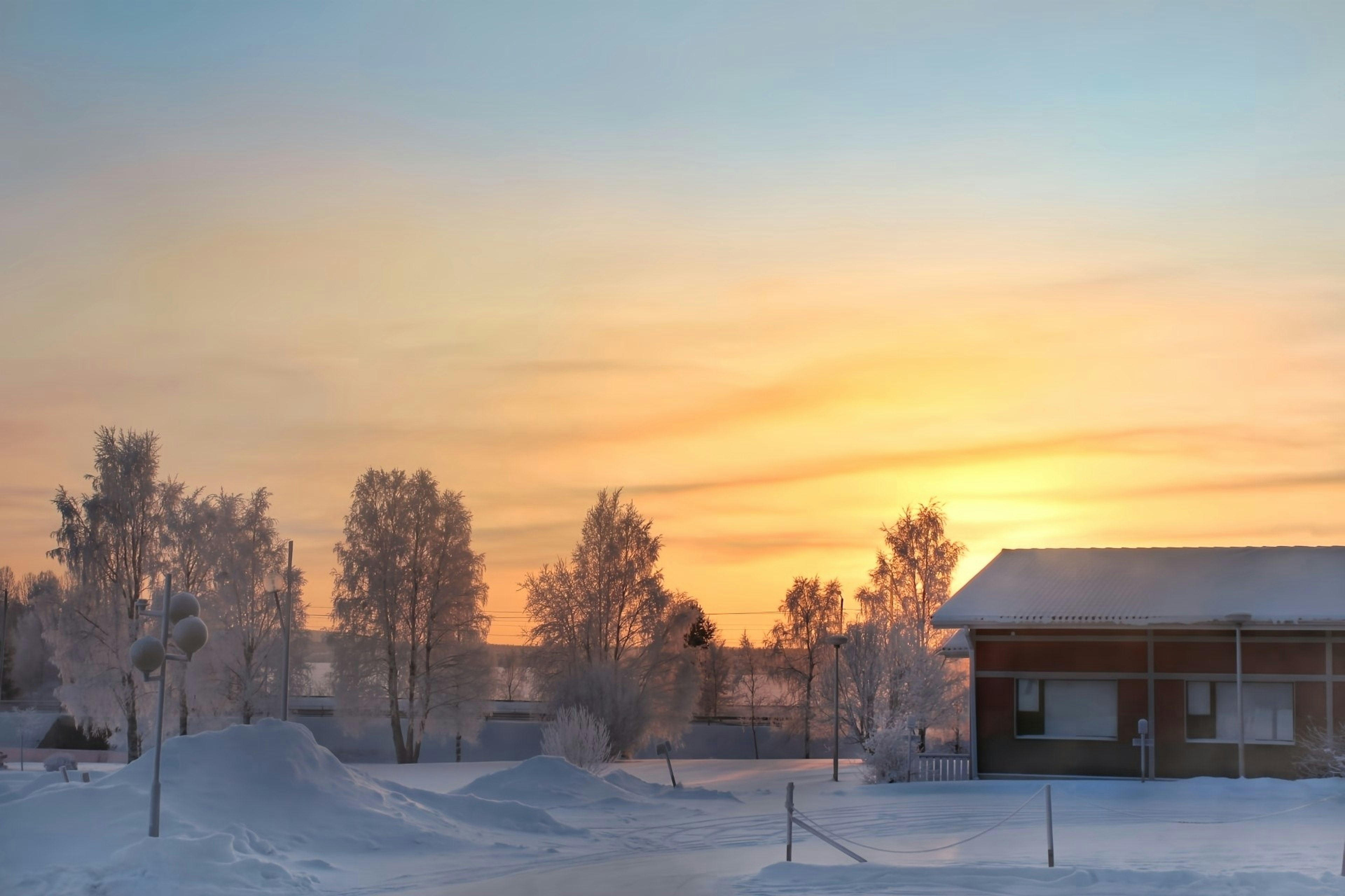 Winter sunset landscape with snow-covered trees and house against an orange sky