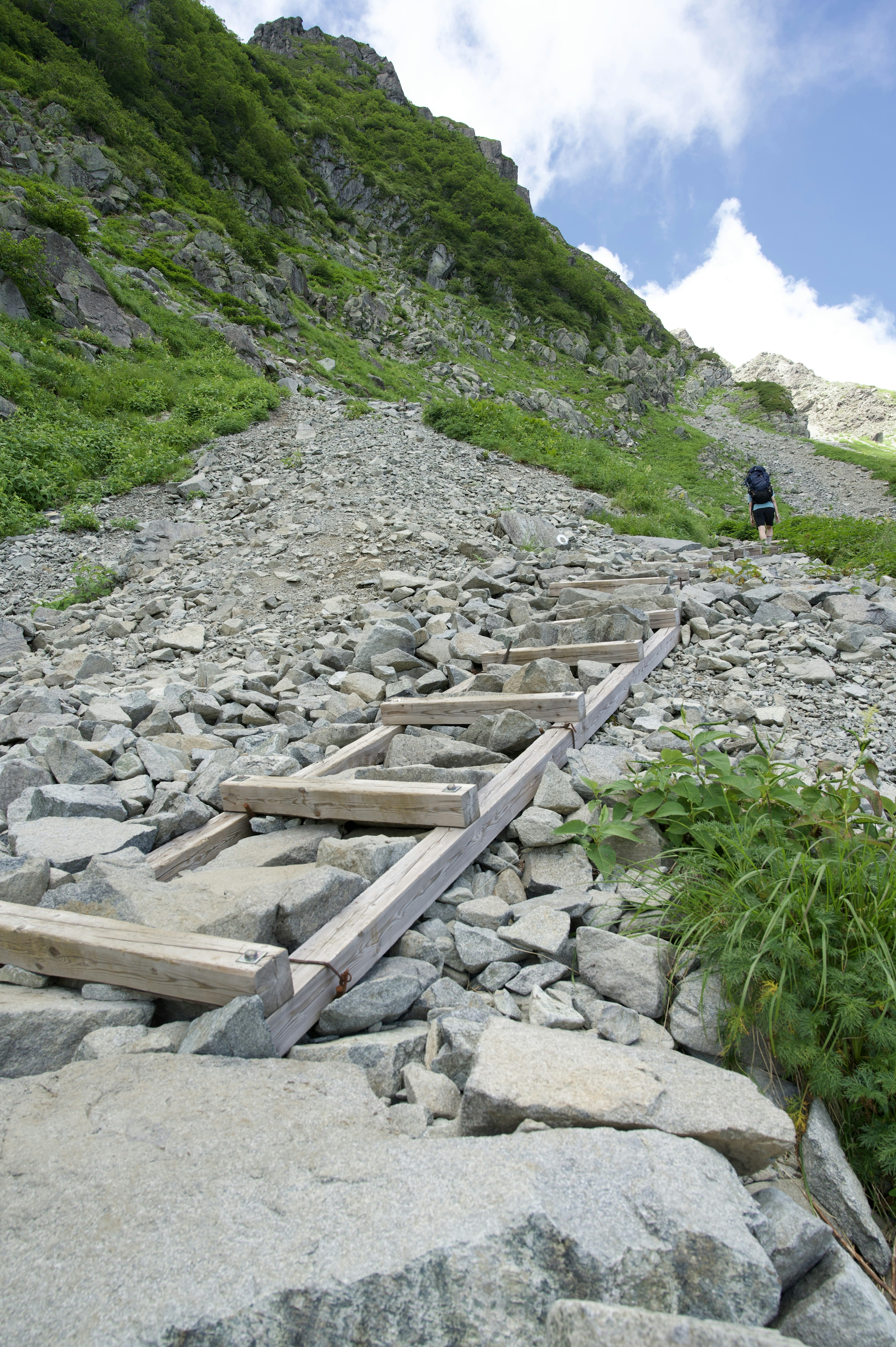 Sentiero montano roccioso con gradini in legno e un escursionista