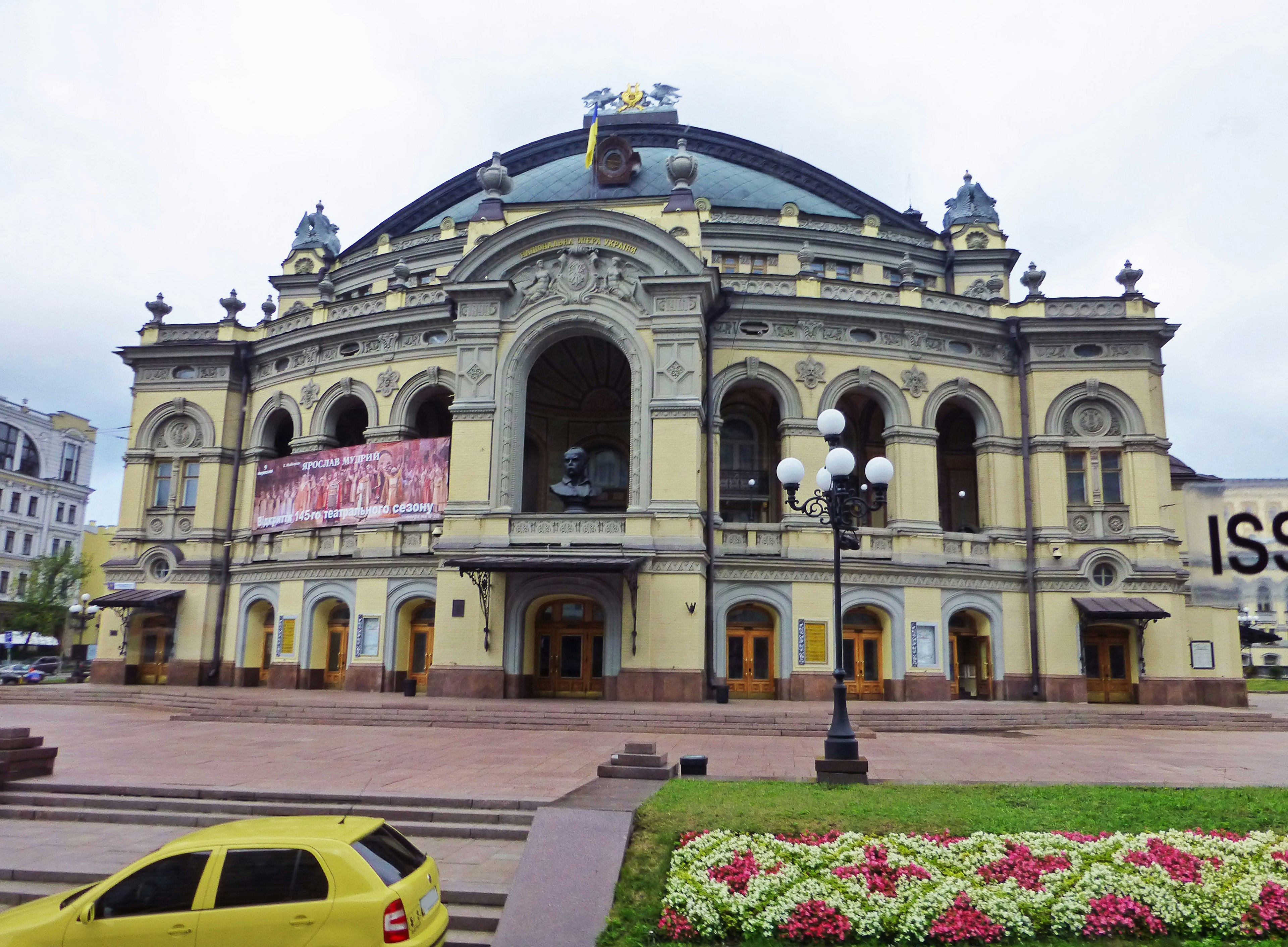 Hermoso teatro de ópera de estilo arquitectónico con un coche amarillo y parterres de flores