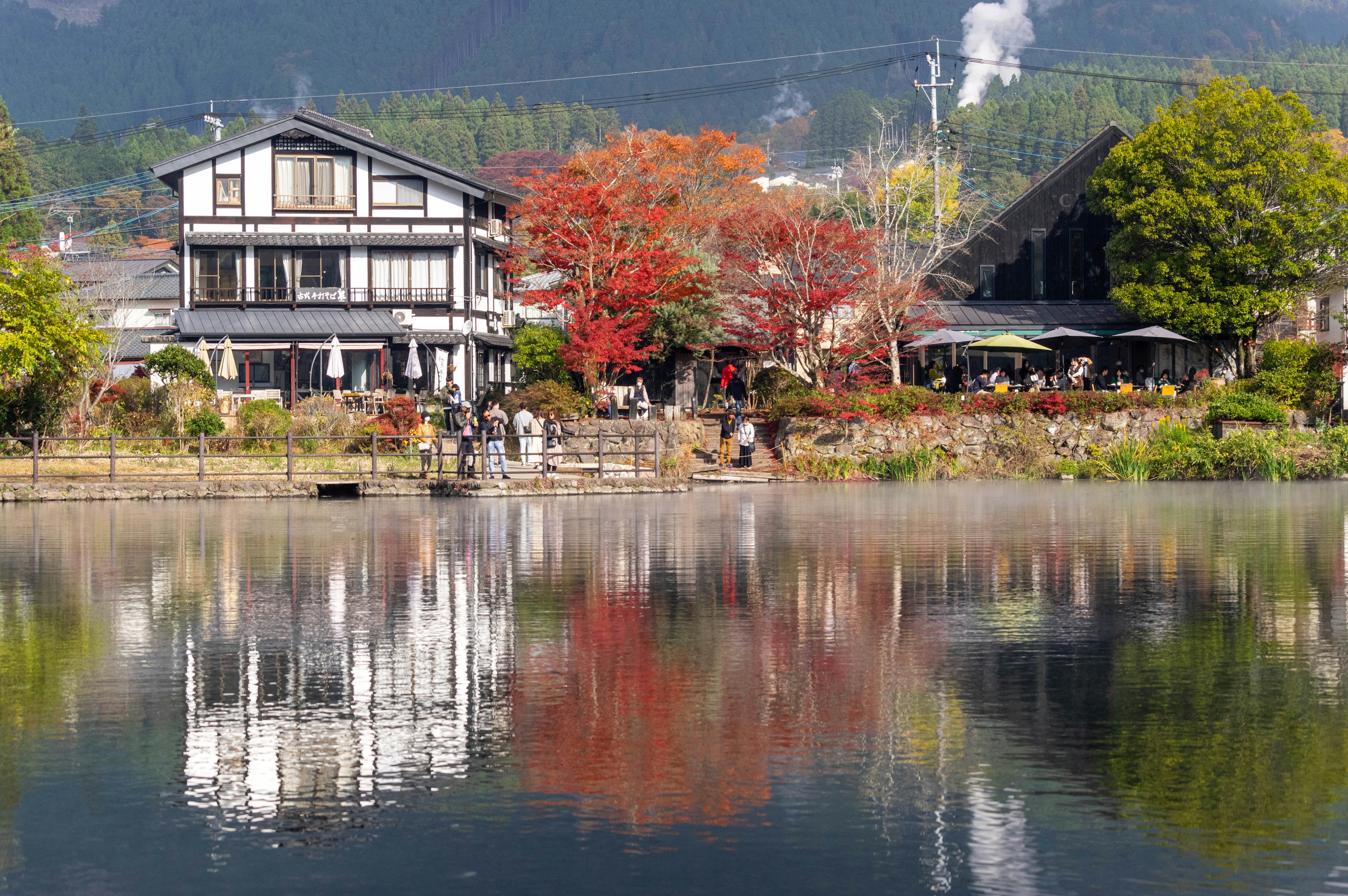 Traditional Japanese house by a serene pond with autumn foliage