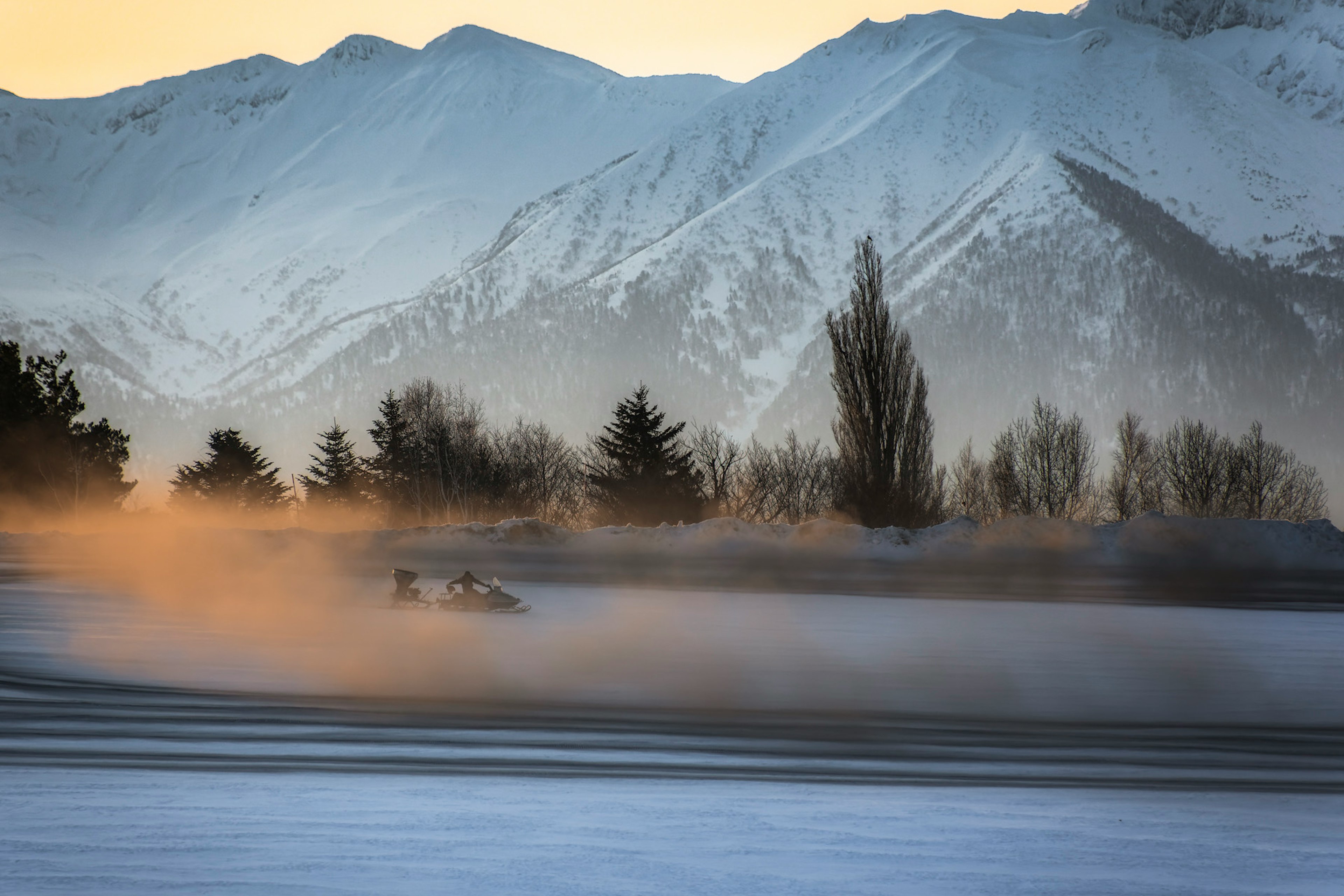 Une voiture roulant sur un paysage enneigé avec des montagnes en arrière-plan