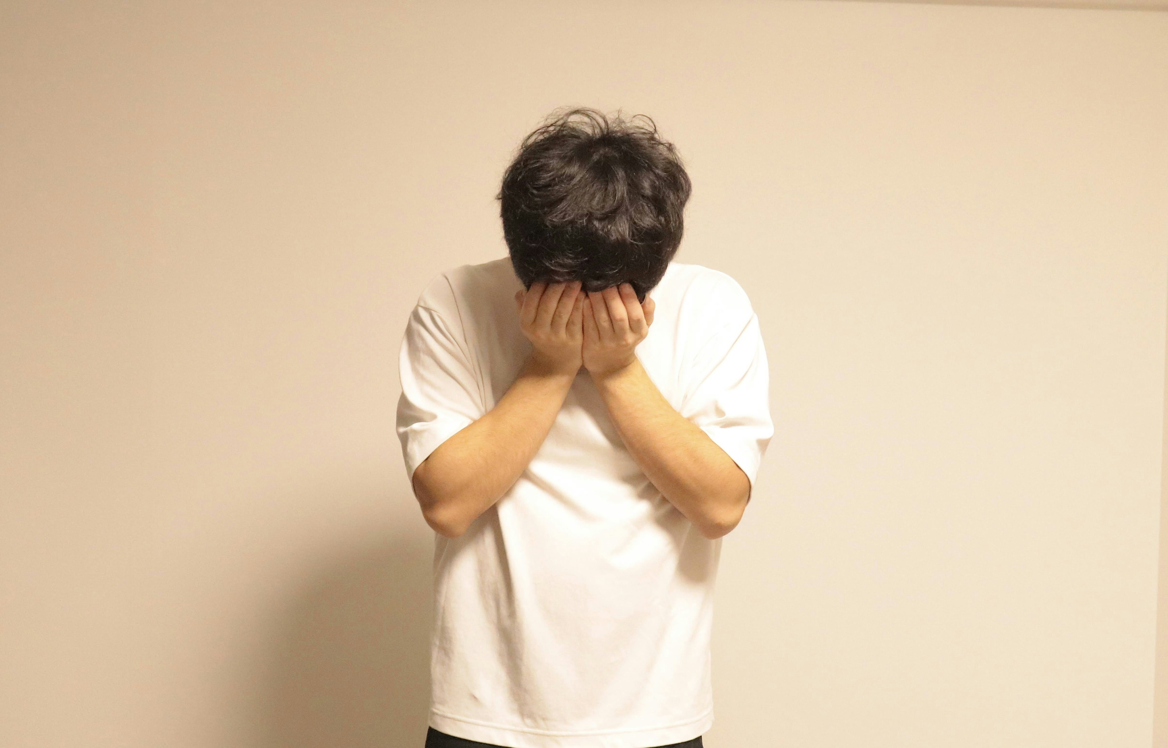 A man in a white shirt covering his face with his hands