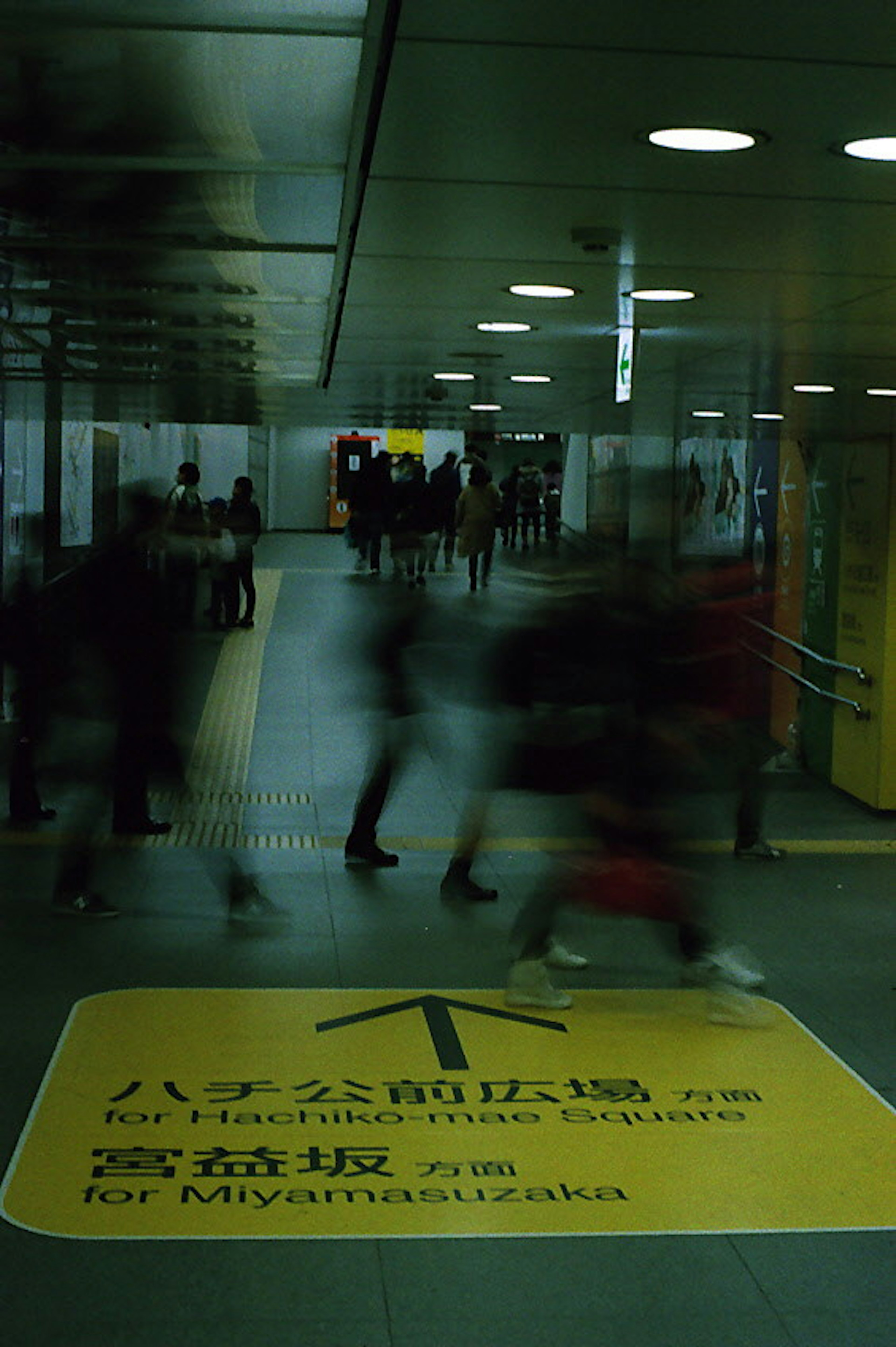 Crowd moving through a train station with a yellow directional sign