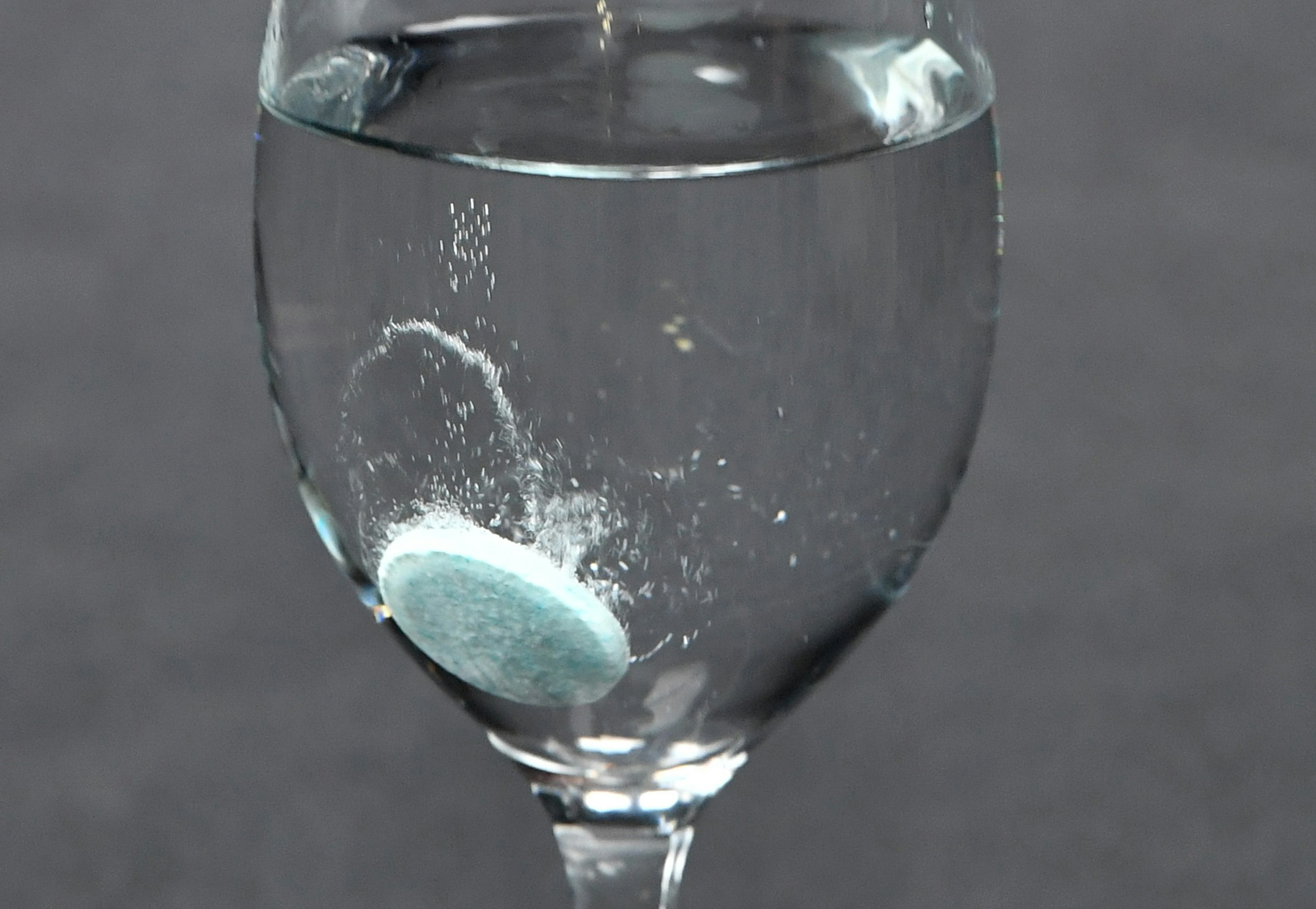 Un verre transparent rempli d'eau et un comprimé bleu en train de se dissoudre