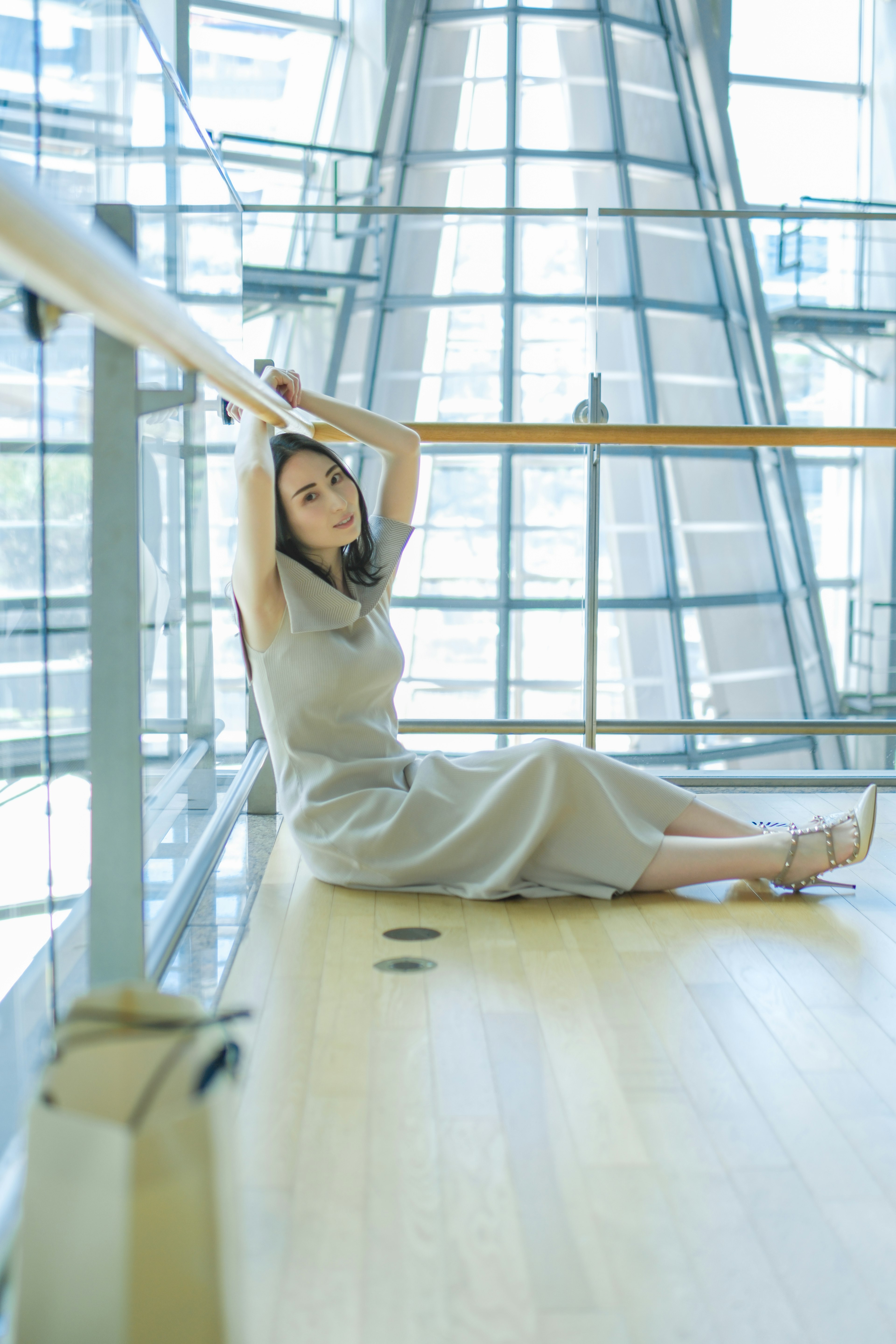 Eine Frau sitzt auf einem Holzgeländer in einem modernen architektonischen Raum und trägt ein graues Kleid