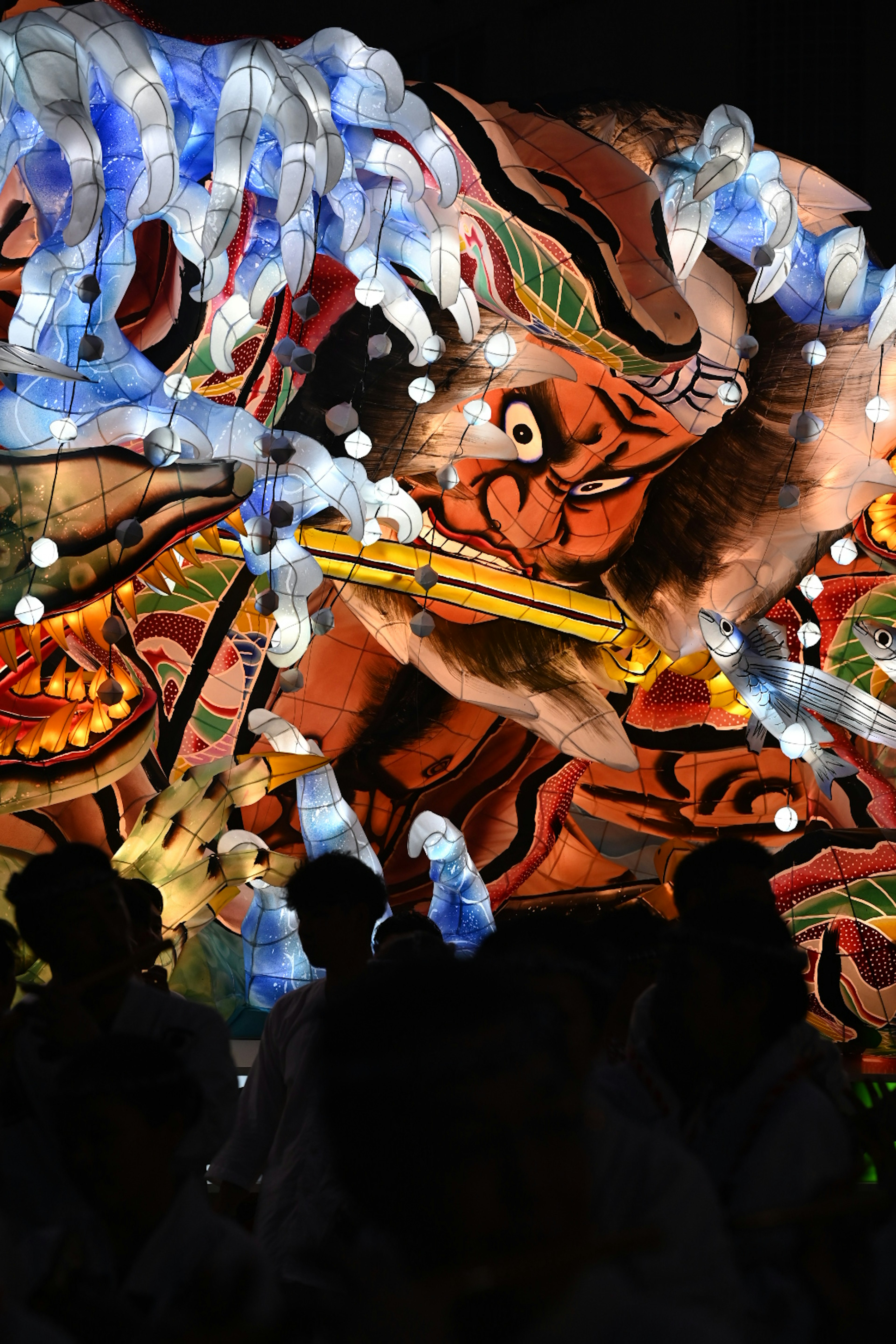 Festival float featuring a tiger illuminated by blue and red lights with silhouettes of people