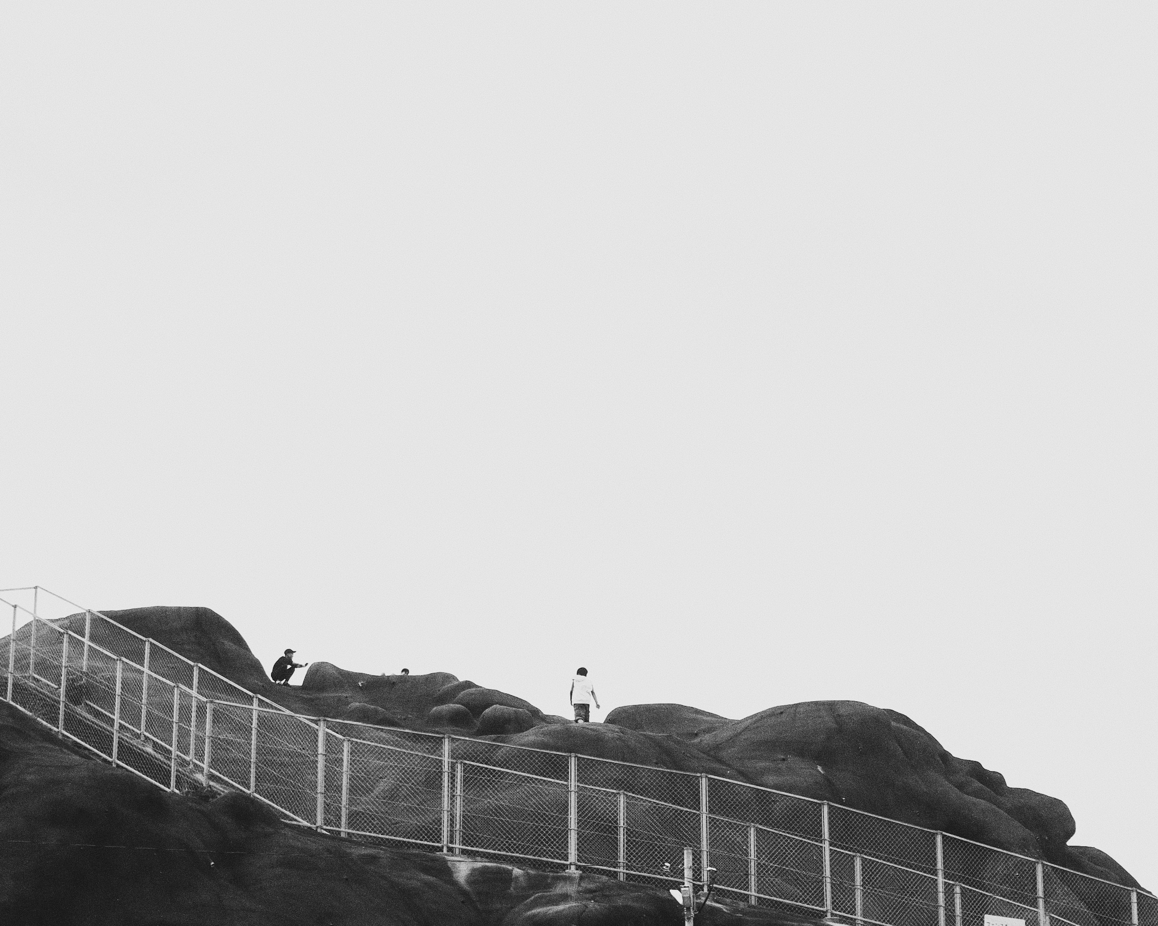 Black and white landscape featuring a large rock surrounded by a fence with people on top