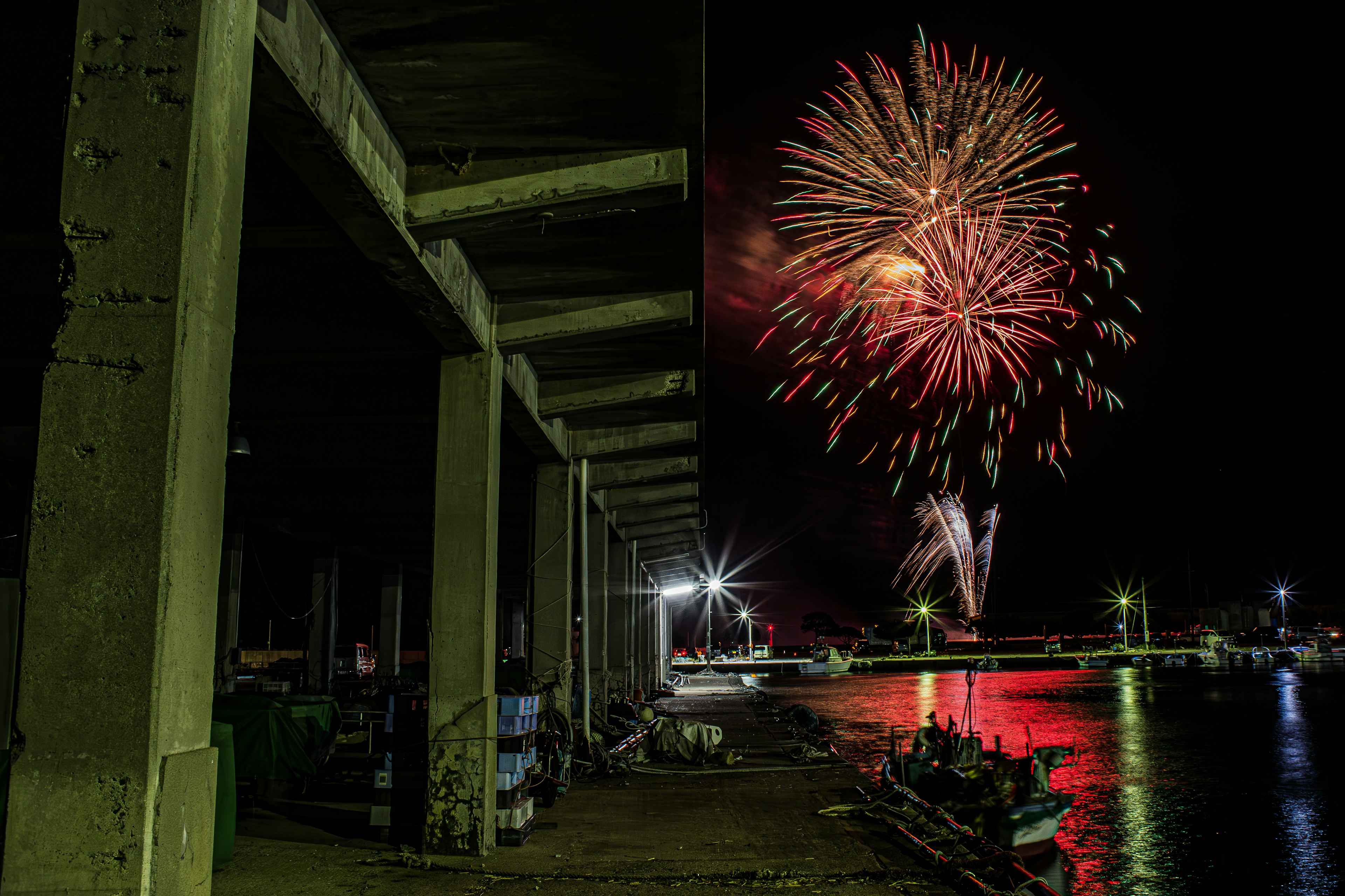 Fireworks lighting up the night sky over a harbor with reflections in the water