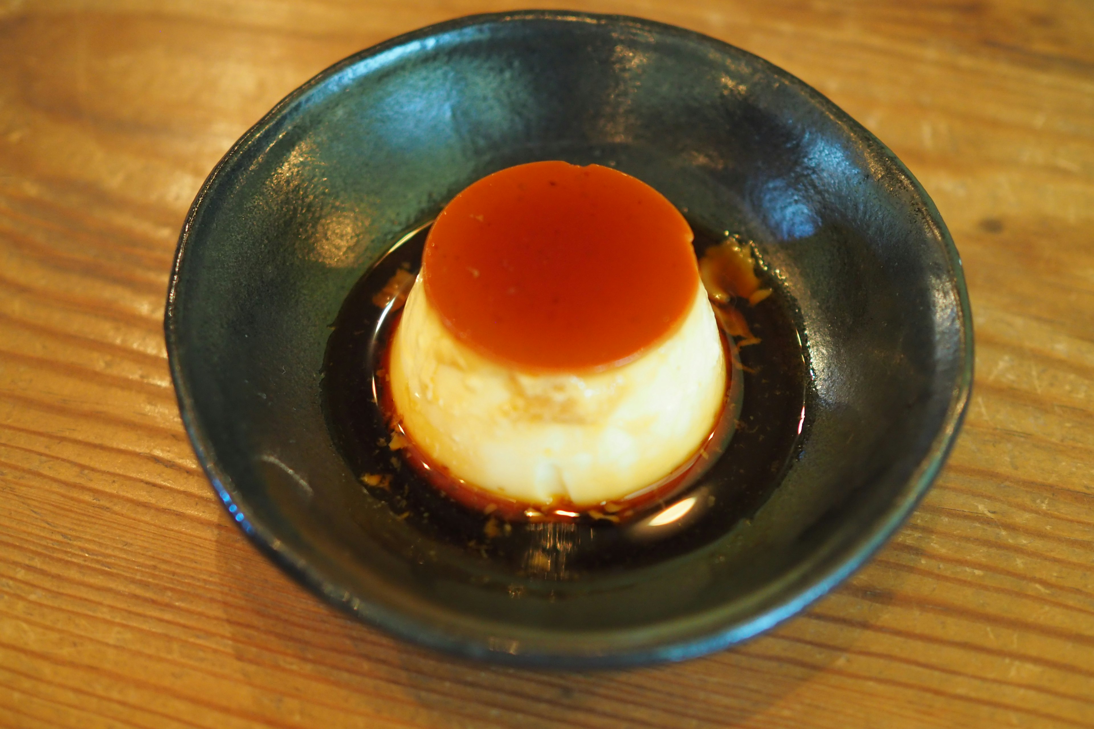 Flan cubierto con salsa de caramelo servido en un plato negro