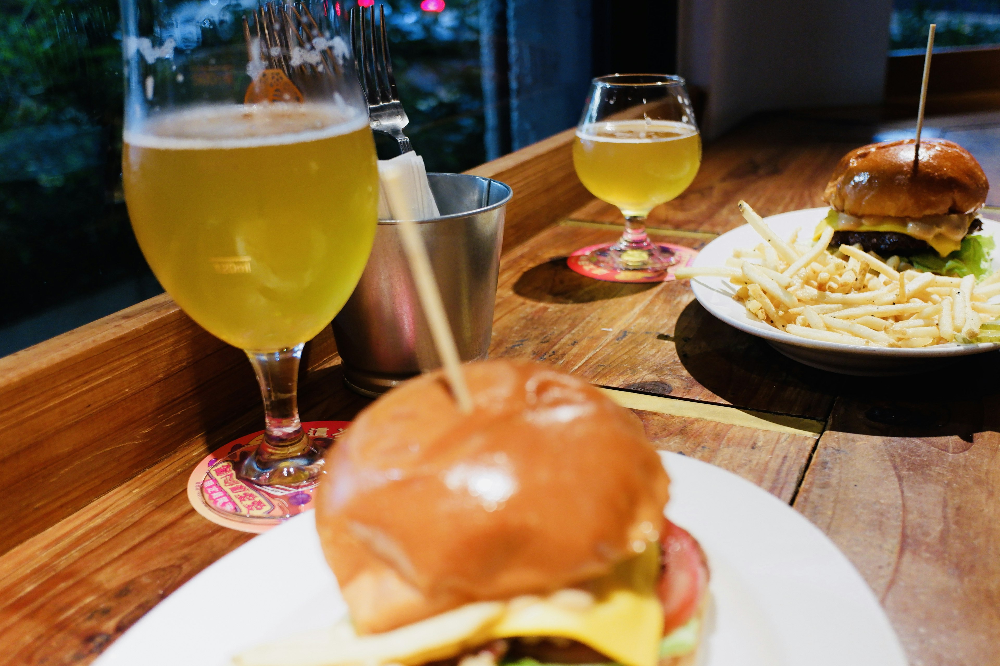 Ein Teller mit einem Burger und Pommes neben Biergläsern auf einem Holztisch