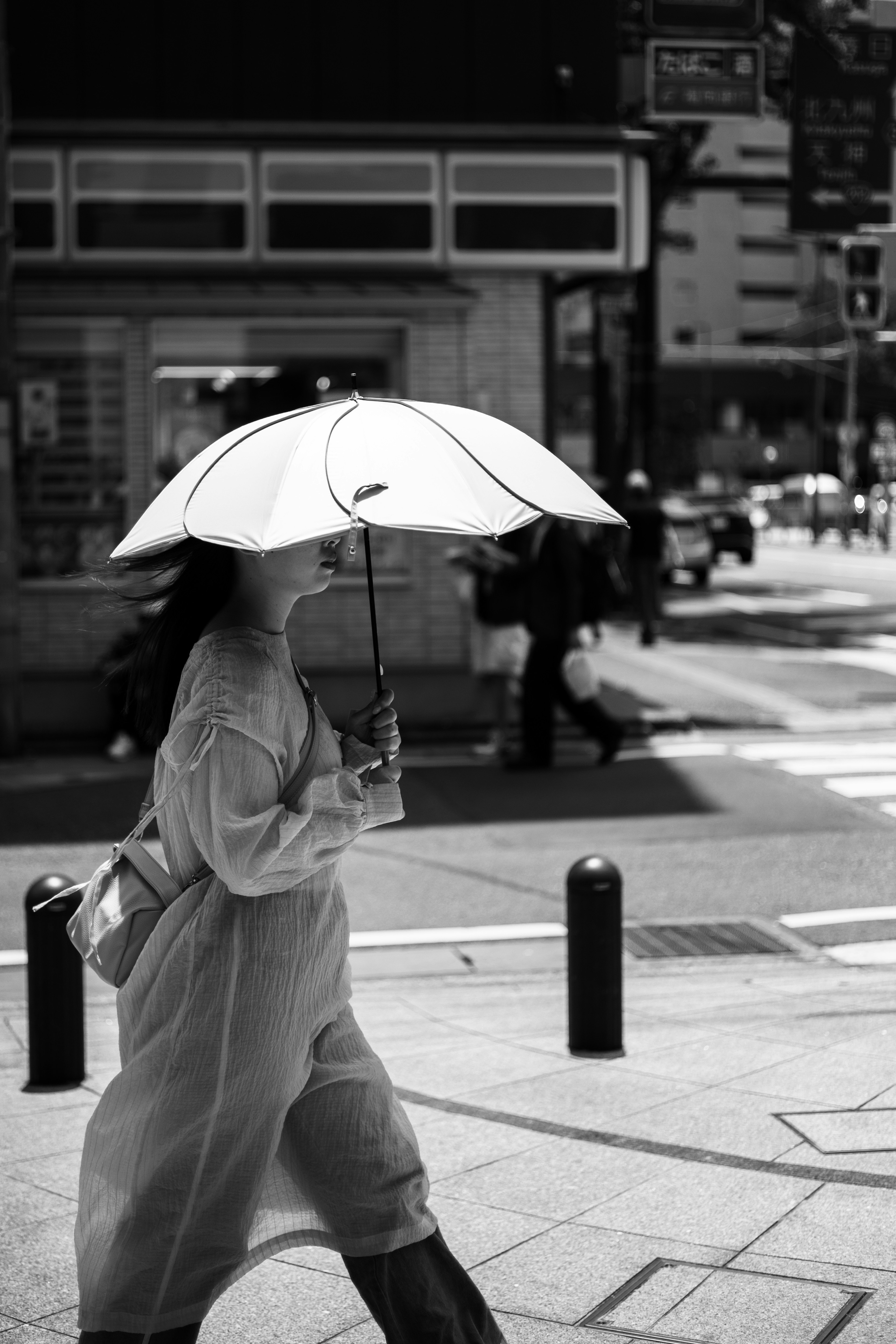 女性が日傘を持って街を歩いているモノクロ写真