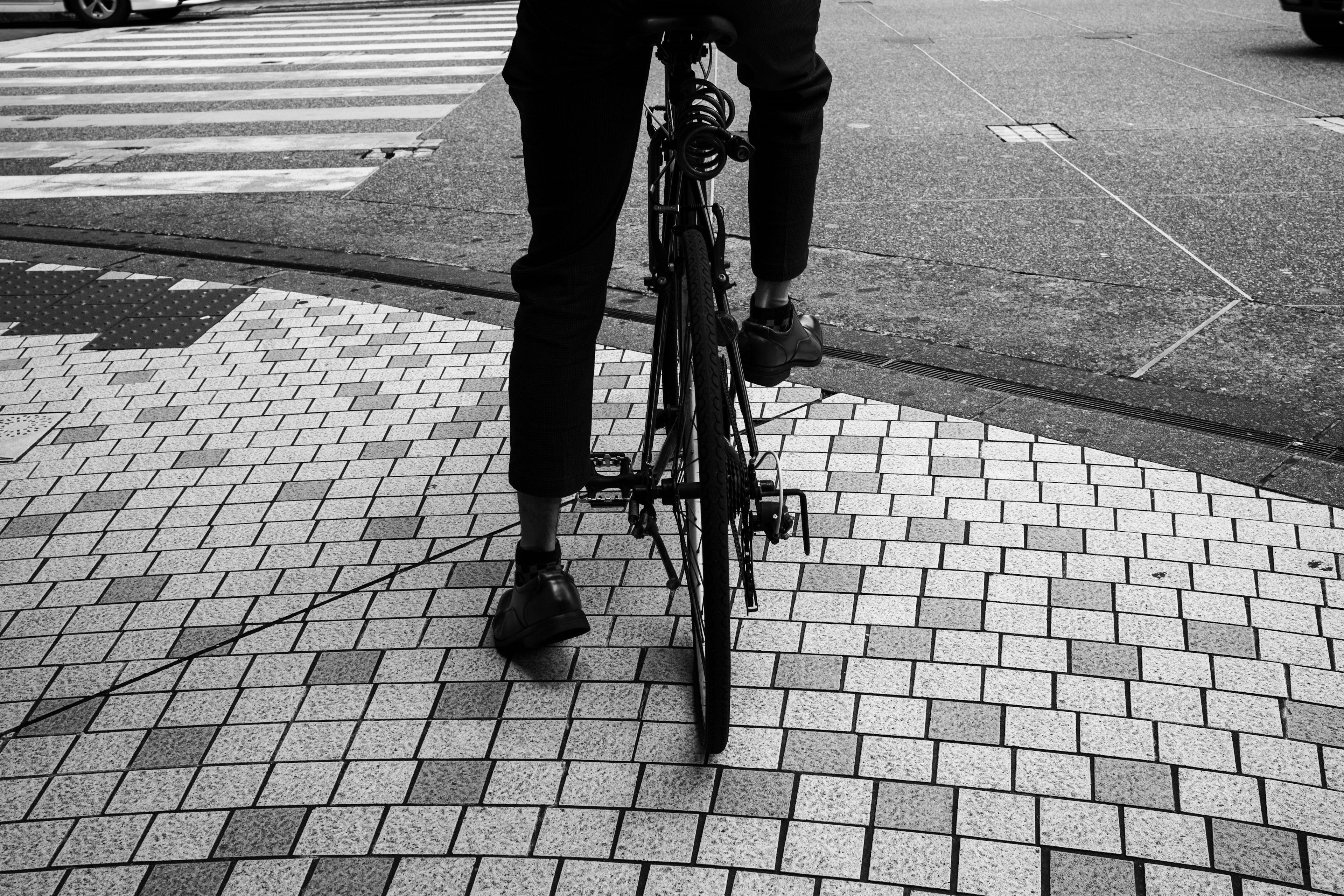 Foto in bianco e nero di una persona in bicicletta che mostra la parte inferiore del corpo con pavimentazione a mosaico sullo sfondo