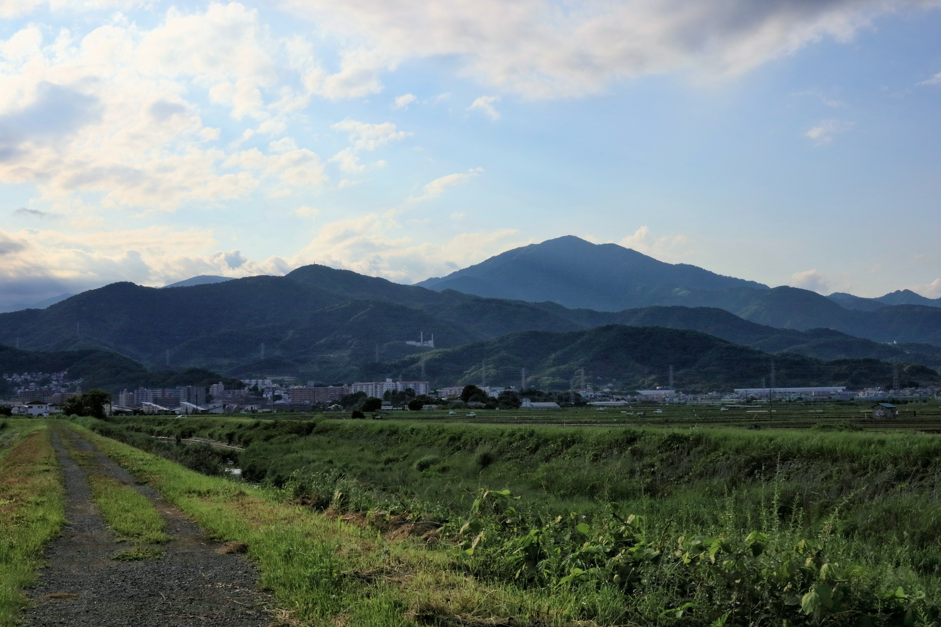 青い空と雲の下に広がる緑の田園風景と山々の景色