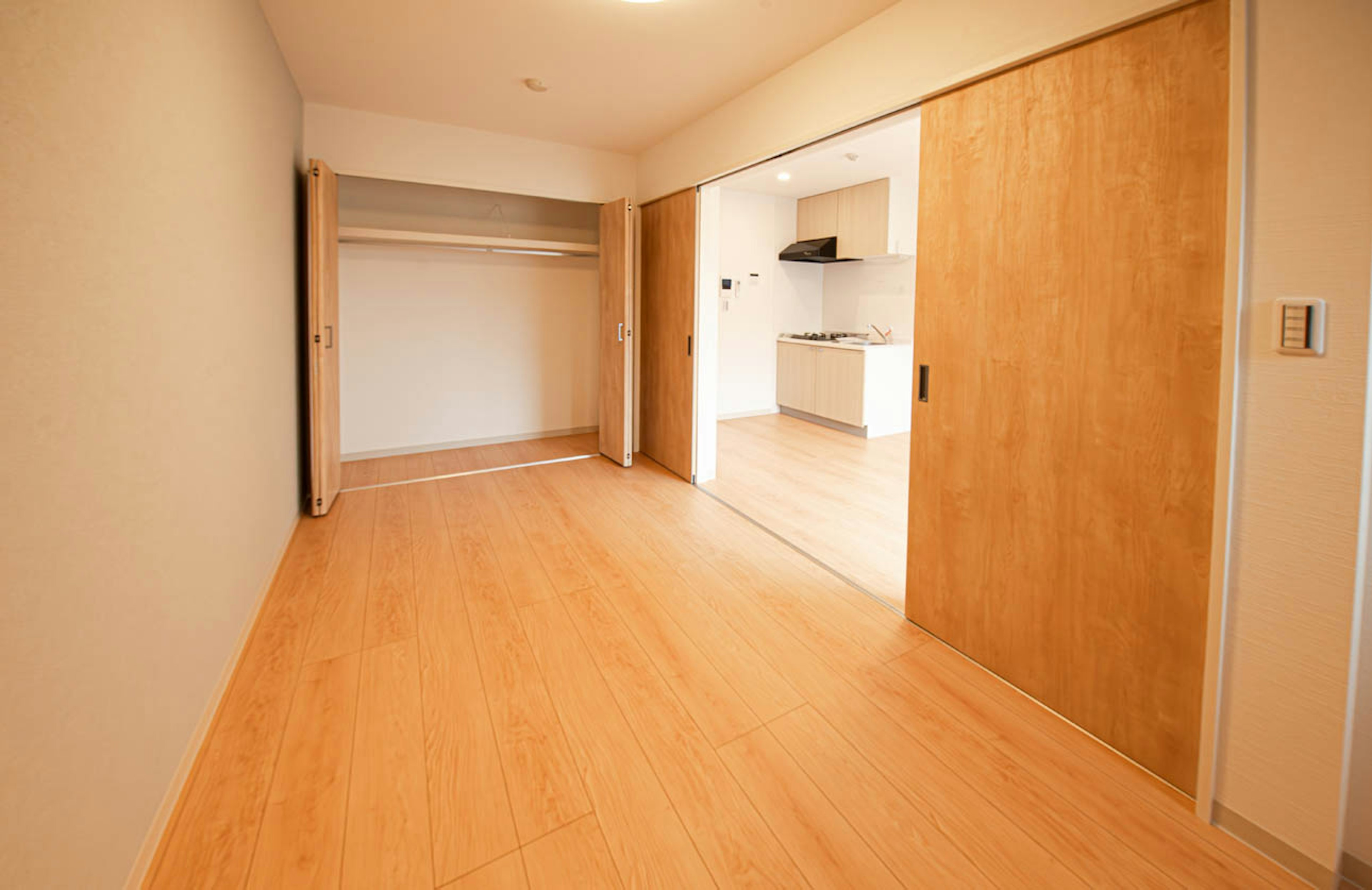 Empty room featuring bright wooden floors with an open layout leading to a visible kitchen