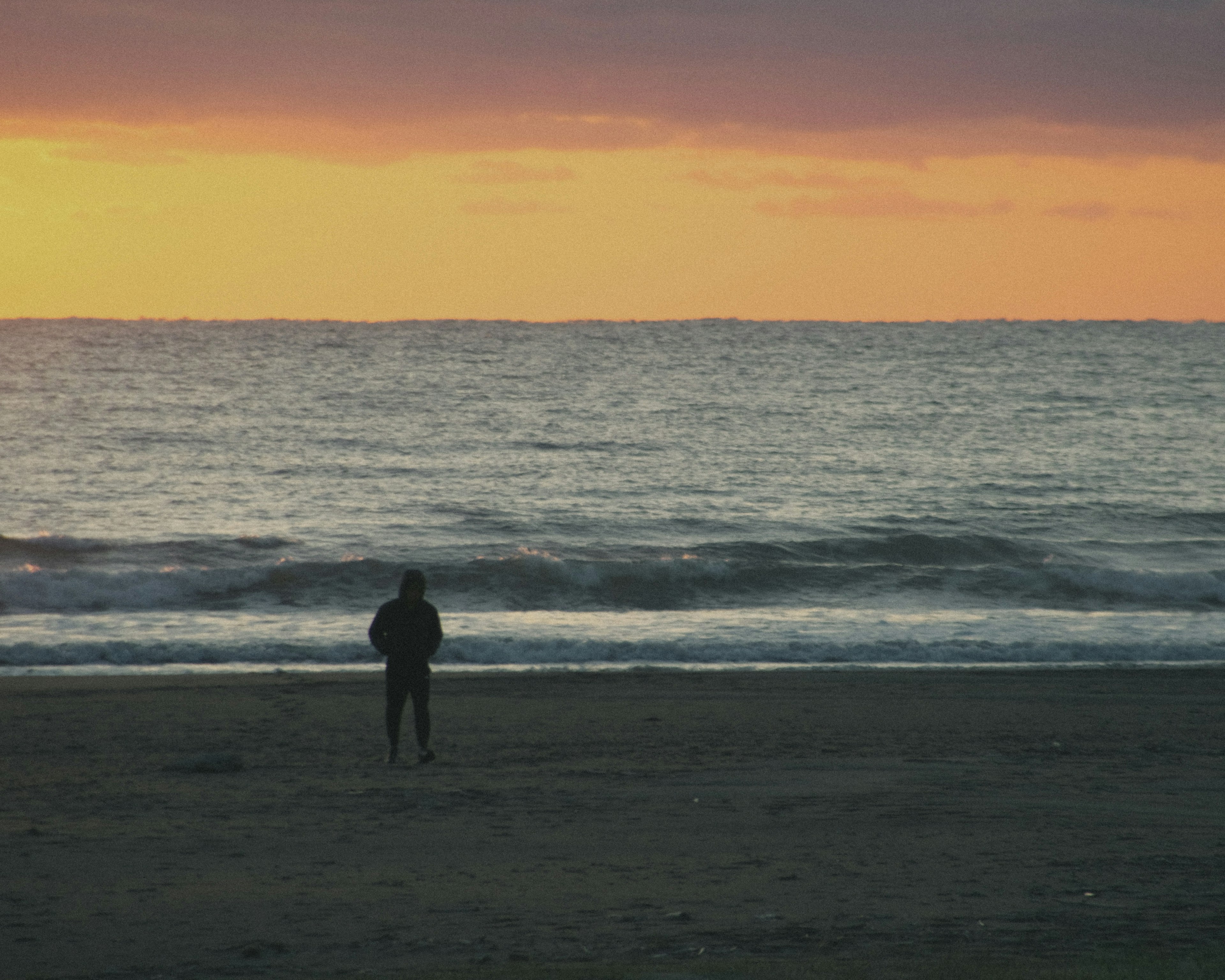 夕日を背景にした海辺で立つ人物