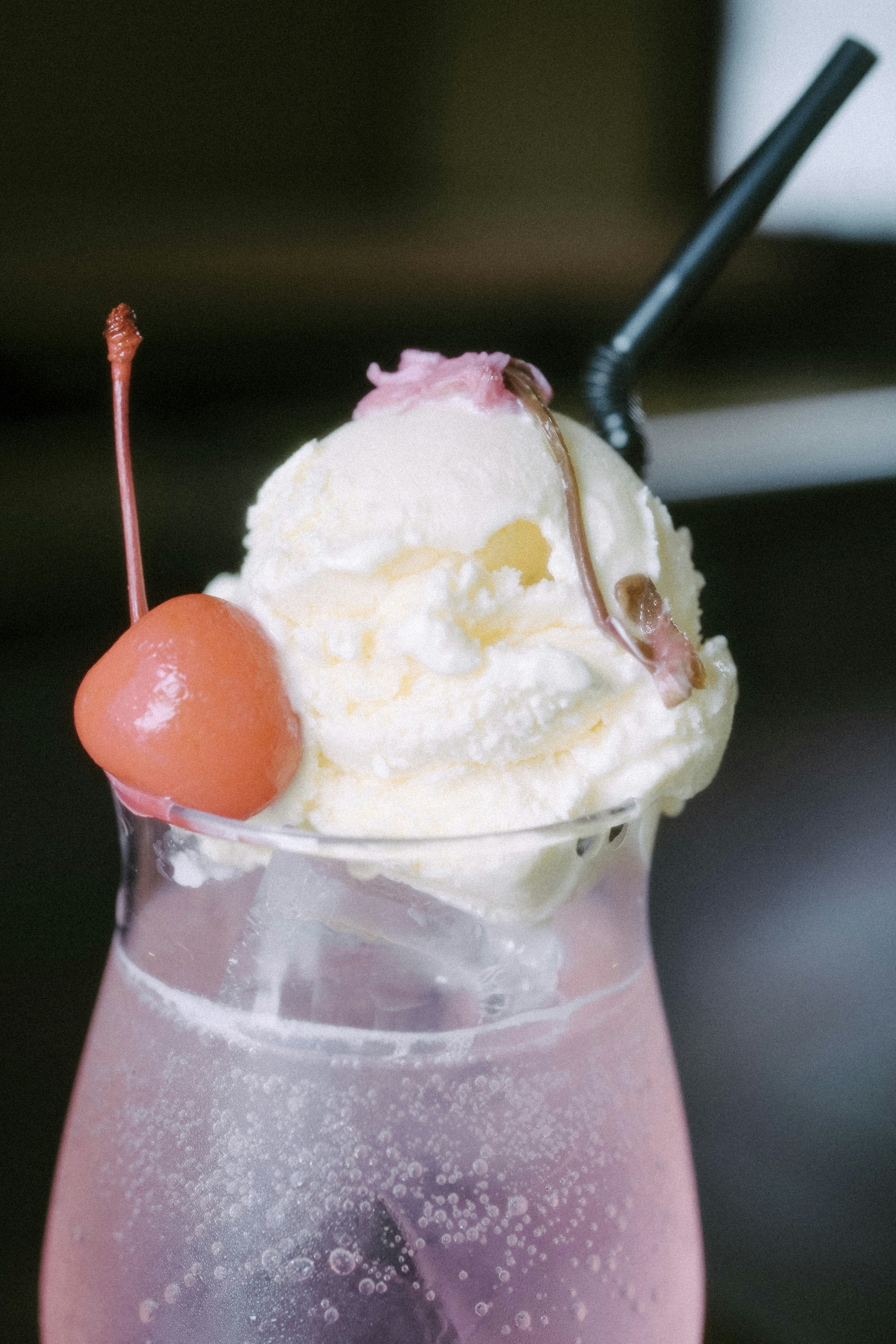 A pink drink topped with ice cream and a cherry