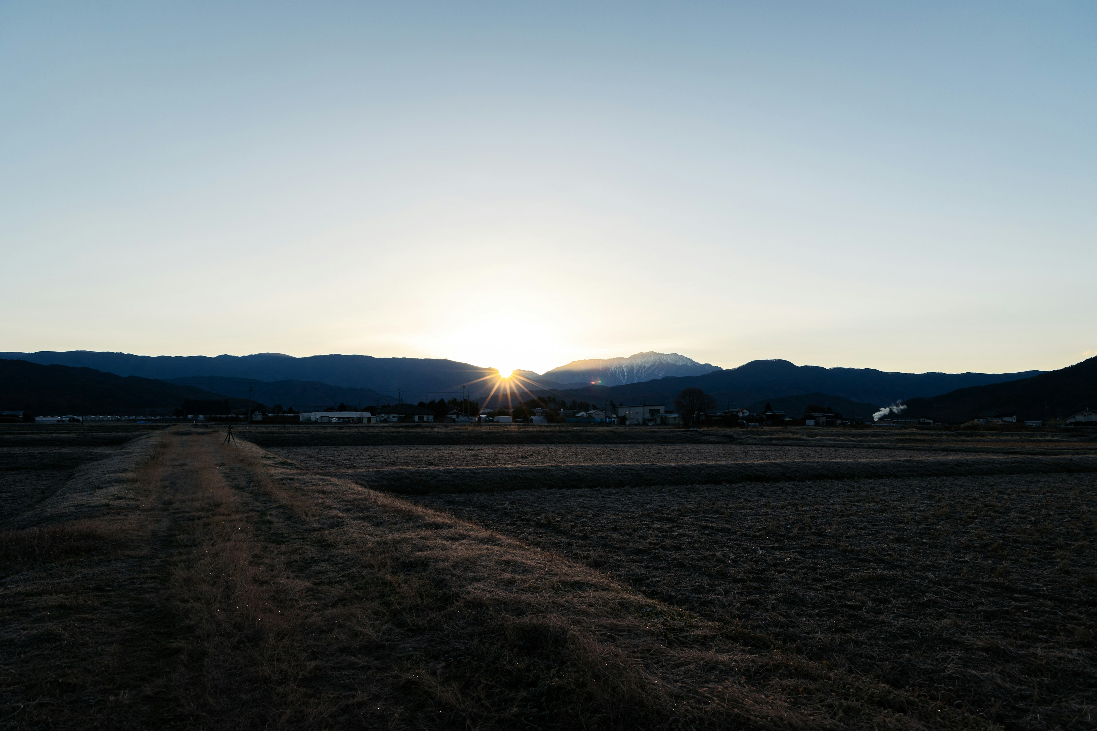 日の出を背景にした山々と田園風景