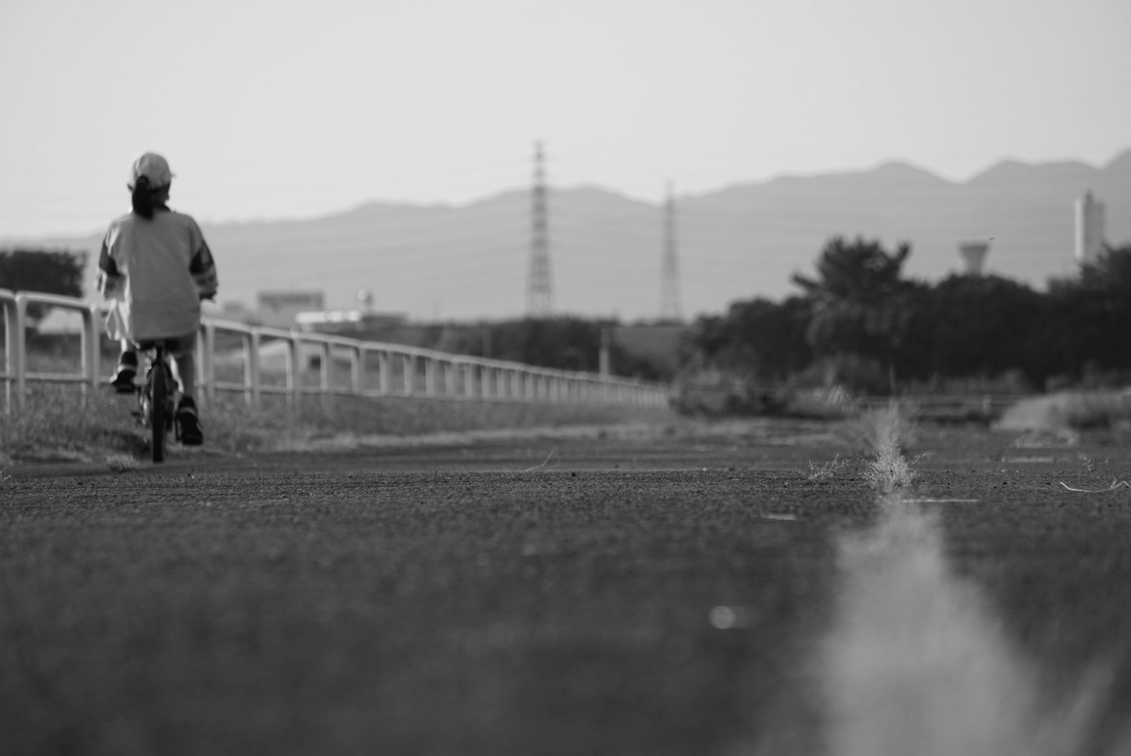 黒と白の写真で自転車に乗る人物が川沿いの道を走っている