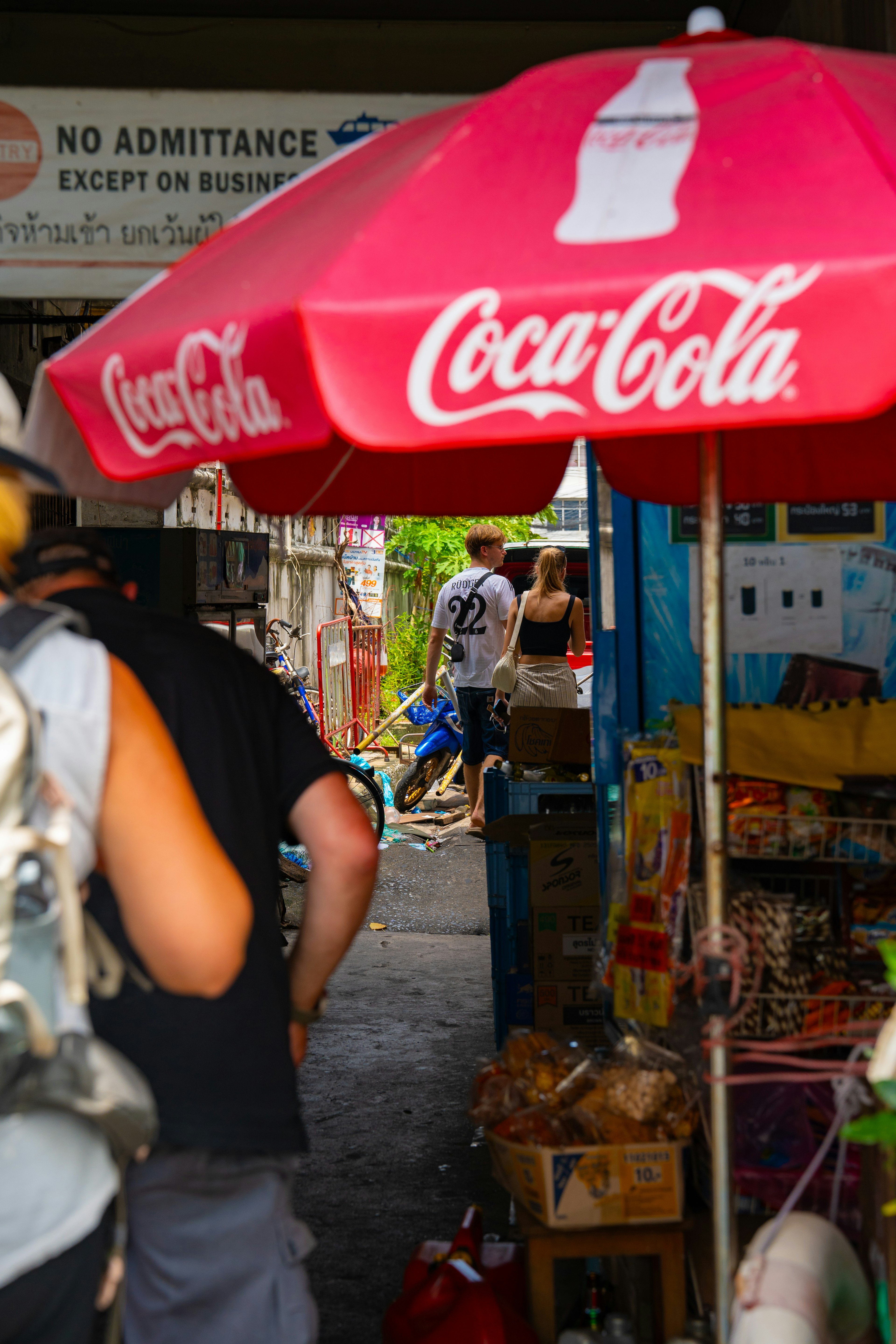 Jalan sempit dengan payung merah Coca-Cola dan pintu masuk toko