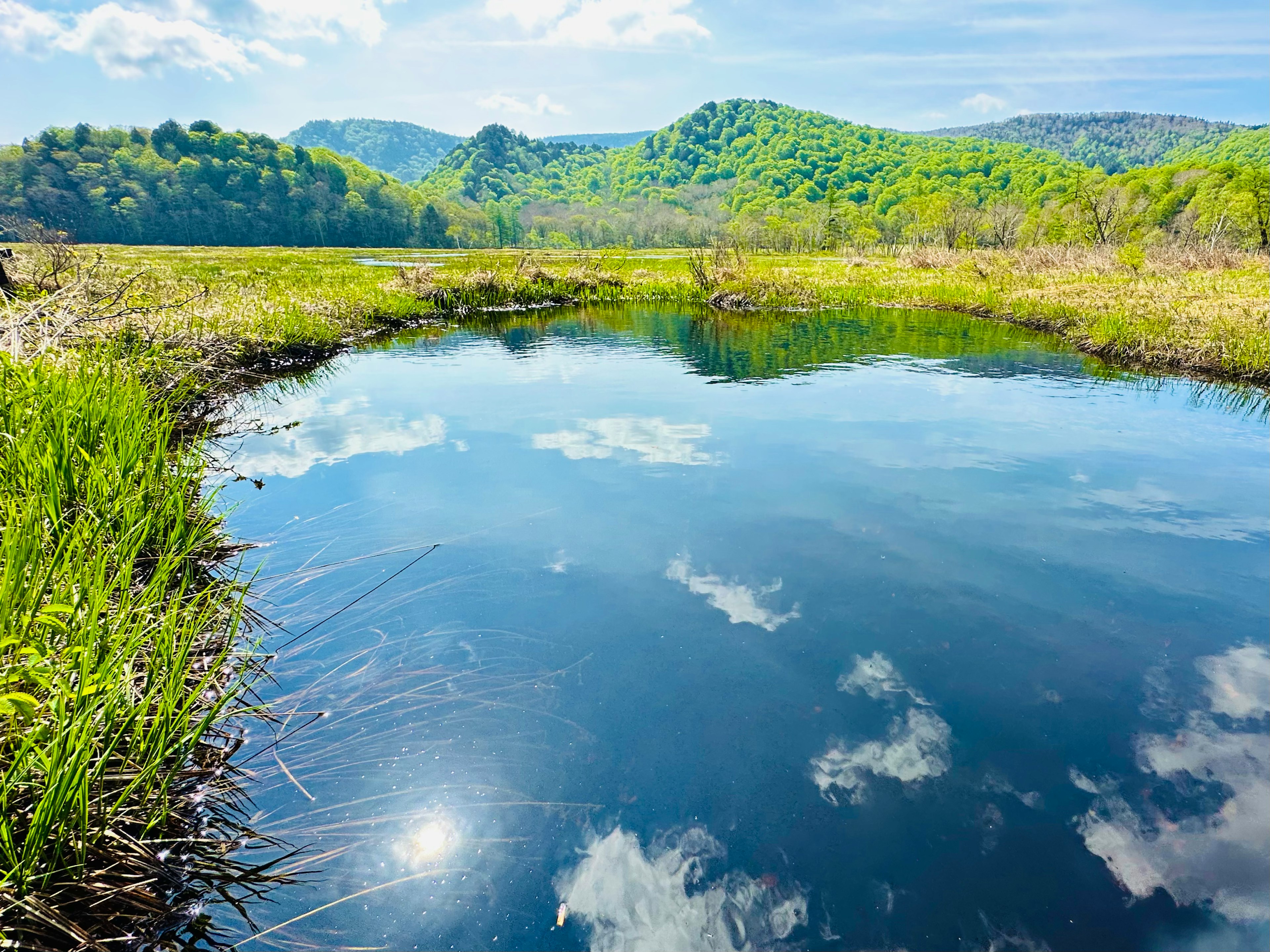 Un estanque sereno que refleja el cielo azul y las nubes rodeado de colinas verdes