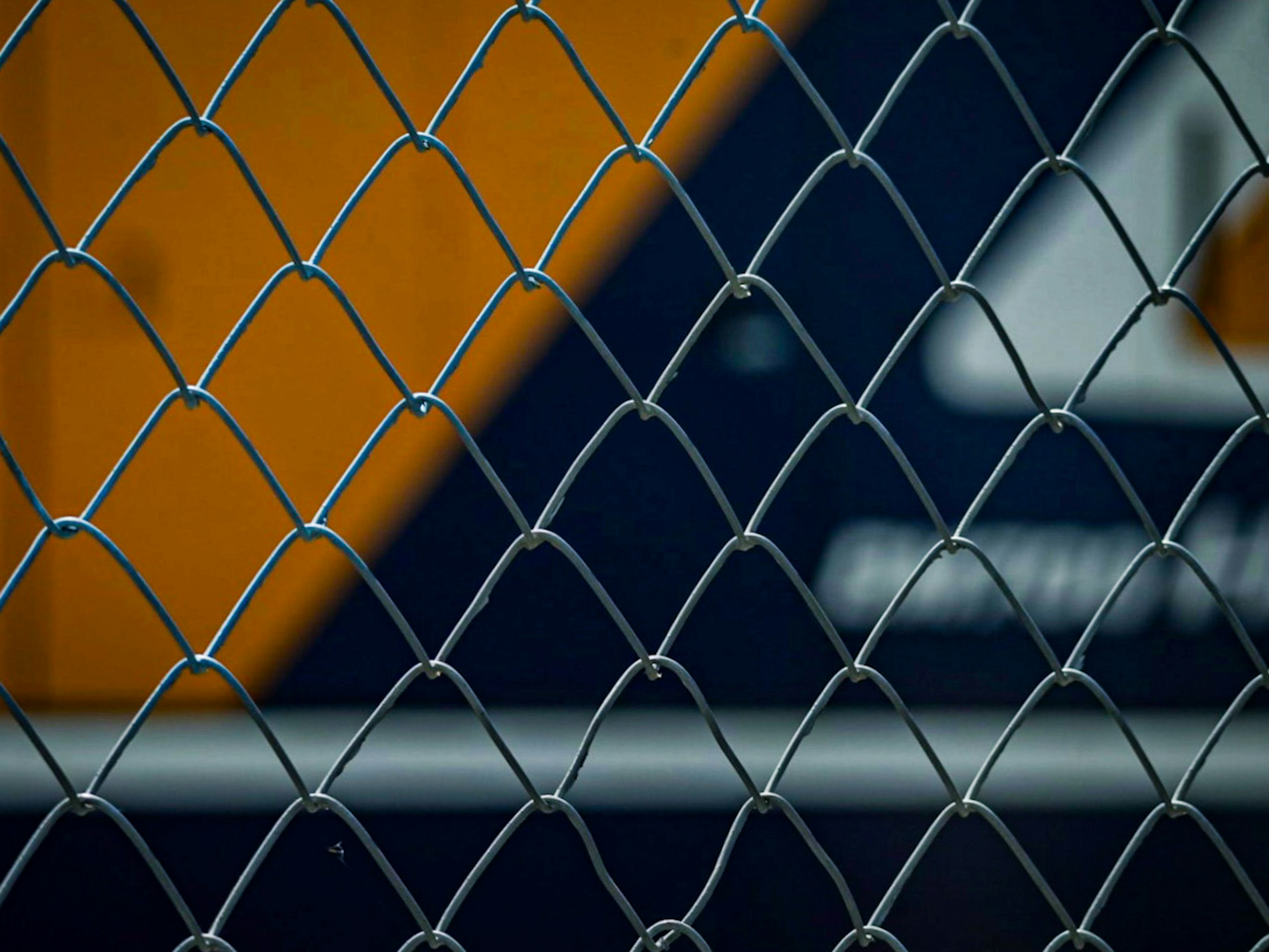 Close-up of a chain-link fence with an orange and blue background