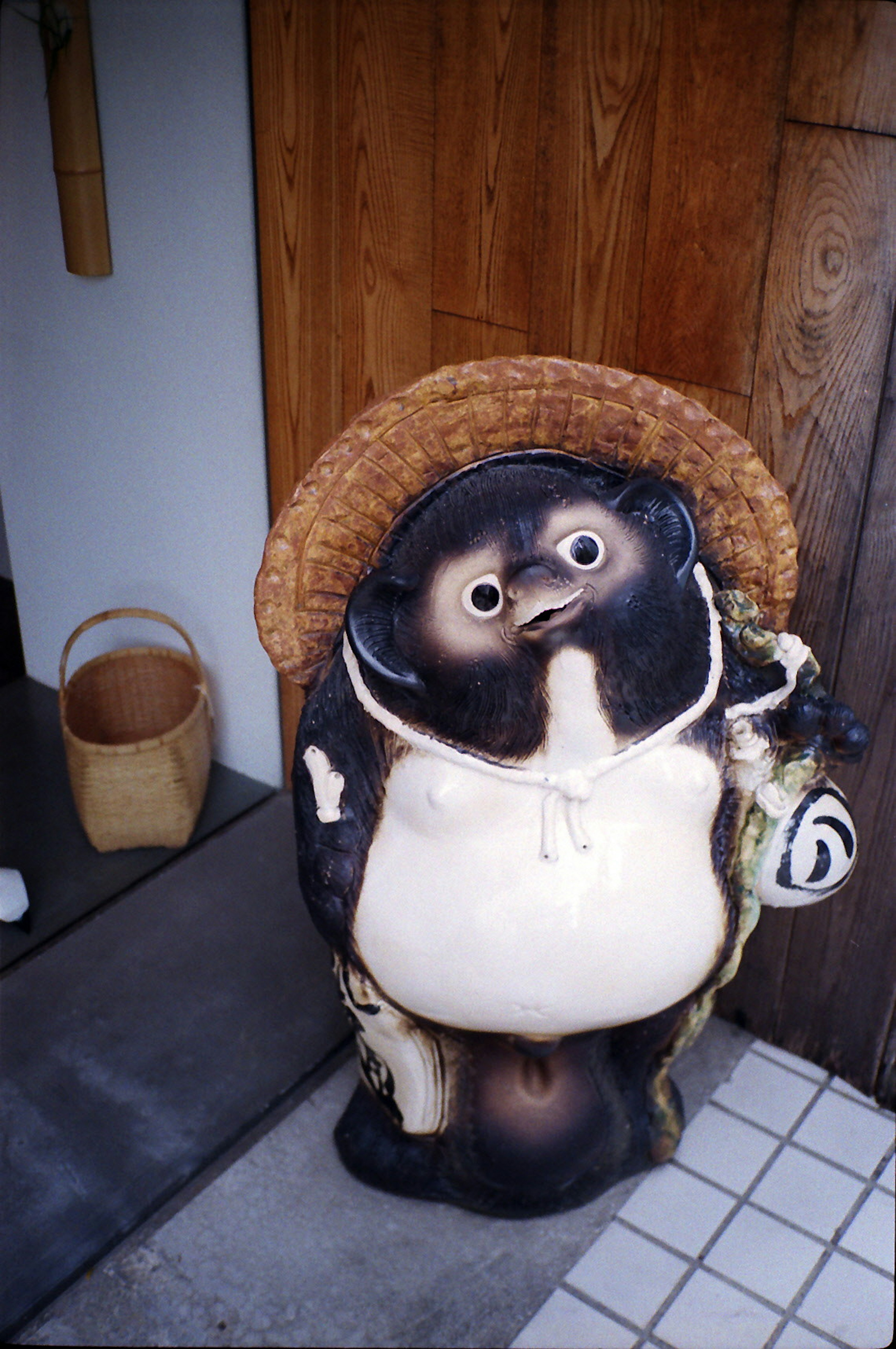 Una estatua de tanuki de ojos grandes con un sombrero de paja y sonriendo