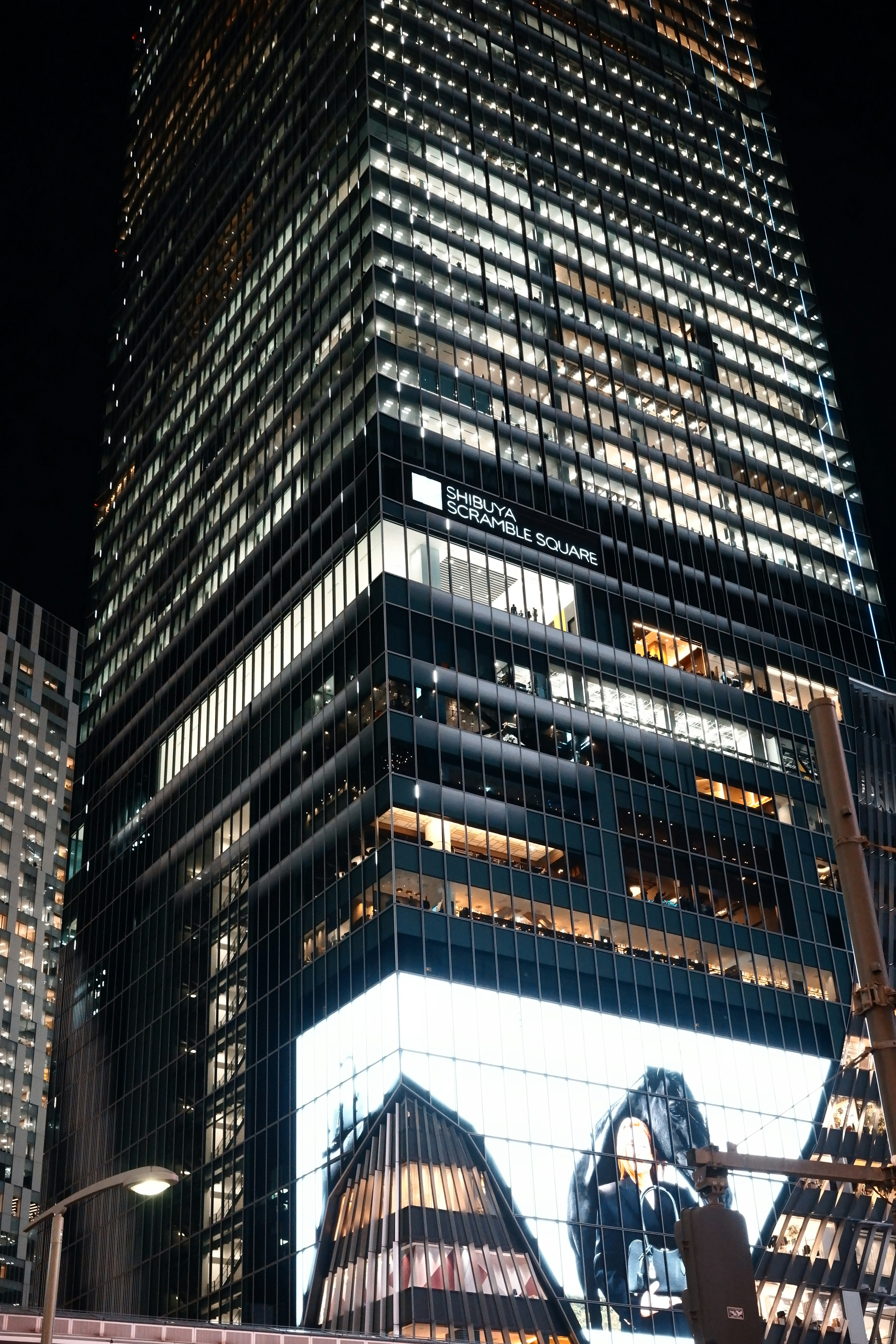 Fassade eines Wolkenkratzers bei Nacht mit hellen Lichtern und einer großen digitalen Werbung