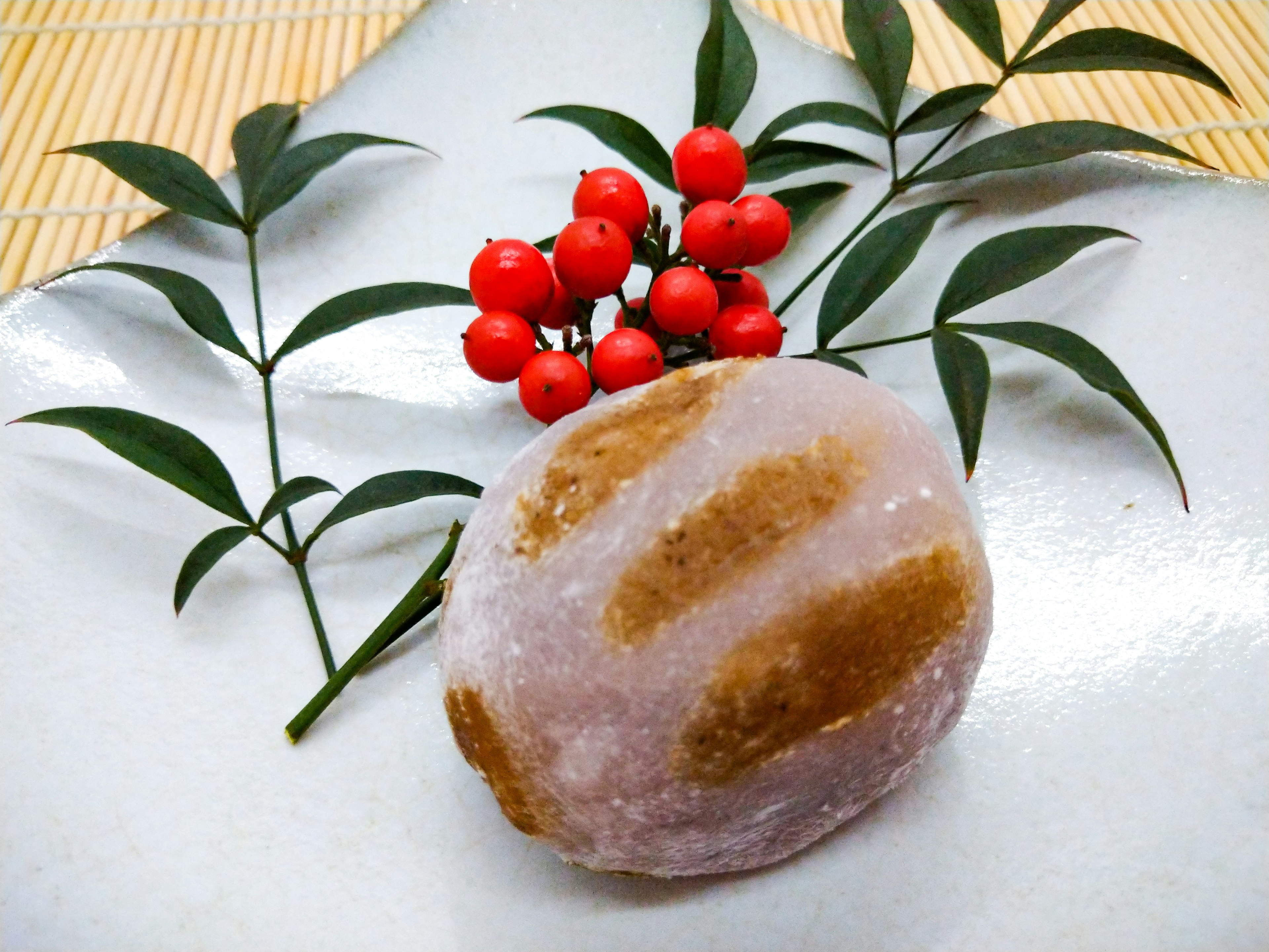 Gambar kue tradisional Jepang di atas piring putih dengan beri merah dan daun hijau