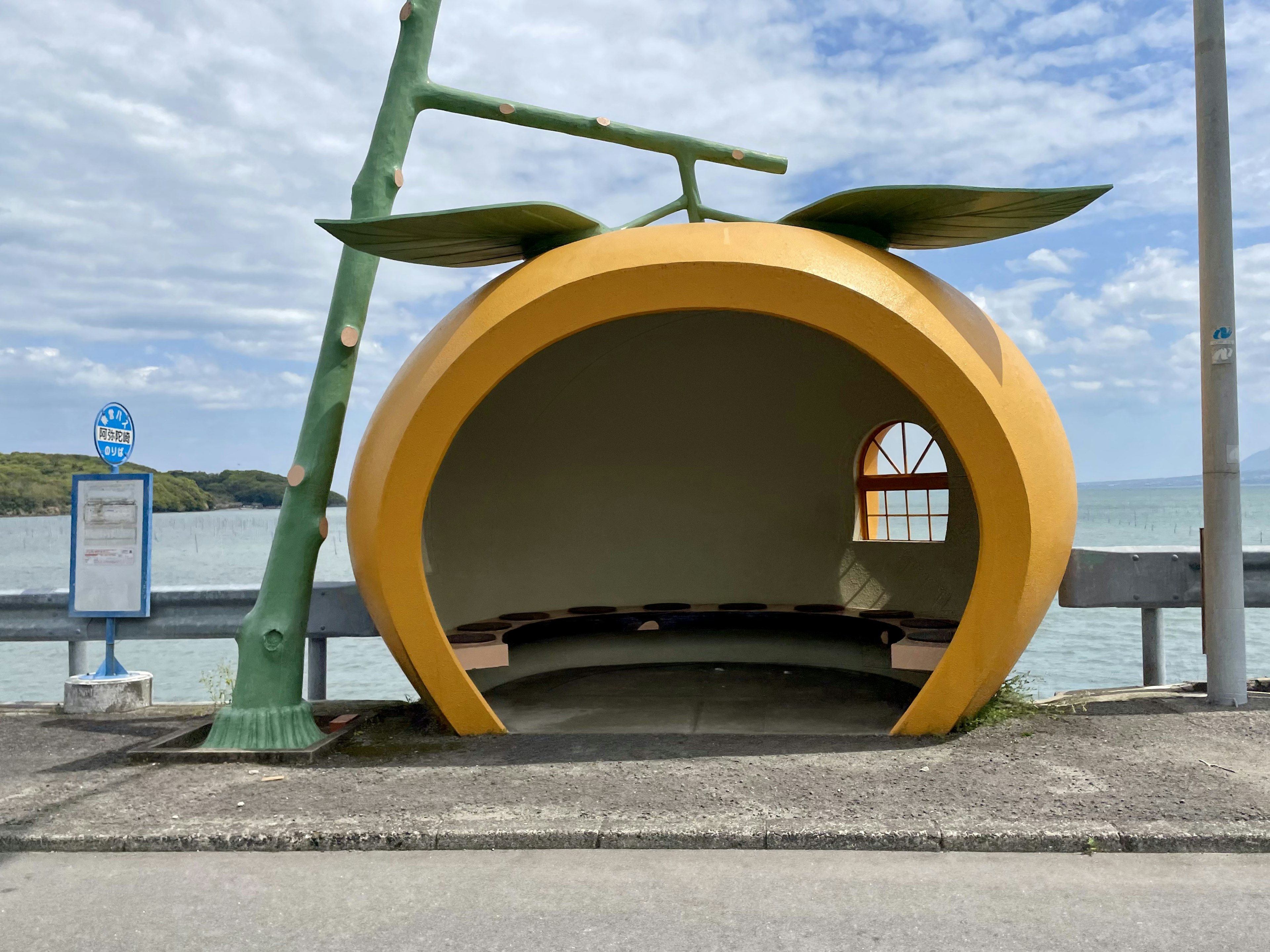 オレンジの形をしたユニークなバス停で青空と海が背景