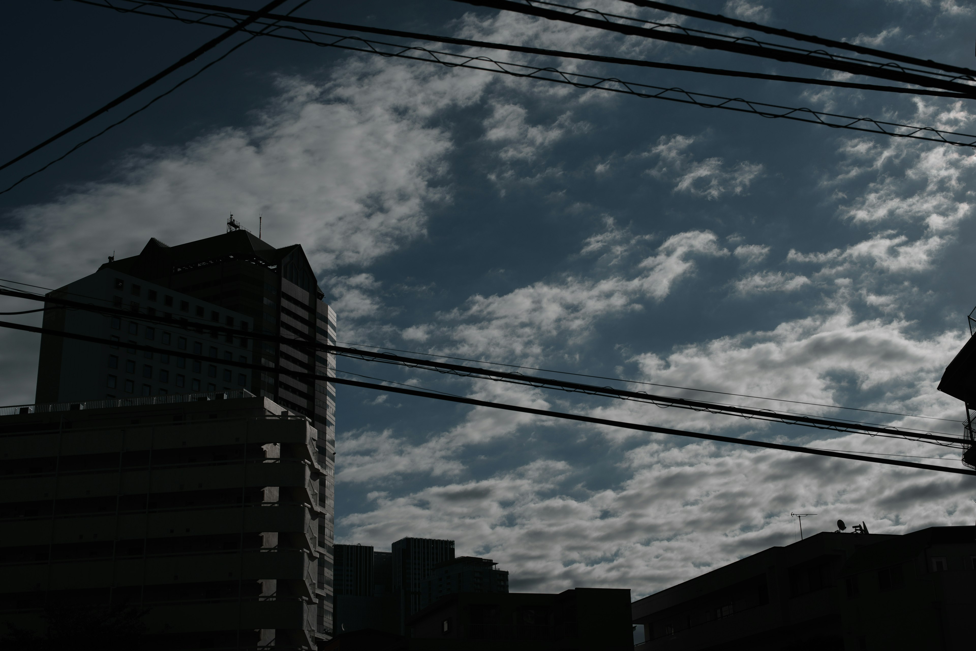 ビルのシルエットと曇り空の写真で、電線が交差している