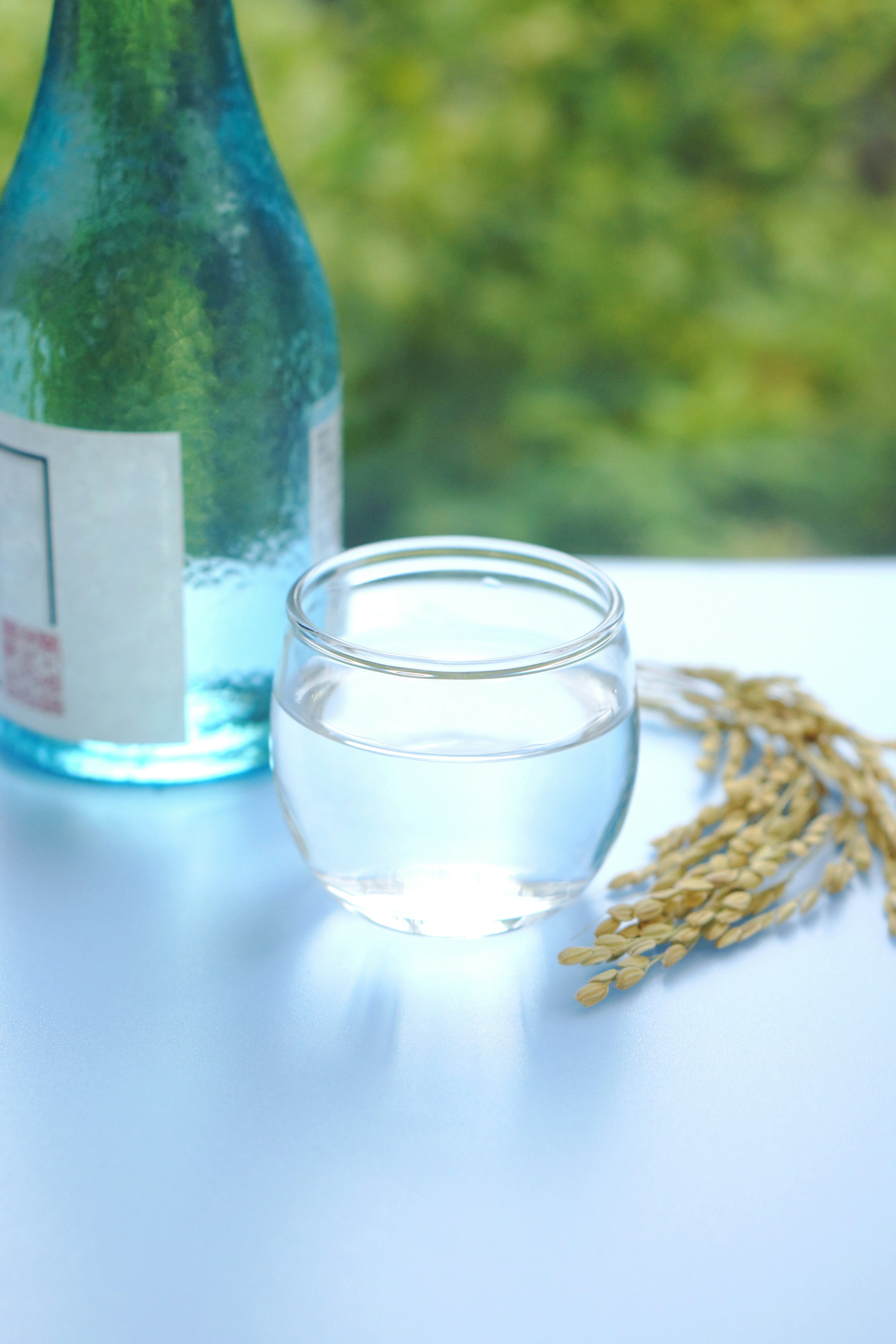 Una bottiglia blu e un bicchiere d'acqua con una spiga di grano accanto in un ambiente sereno