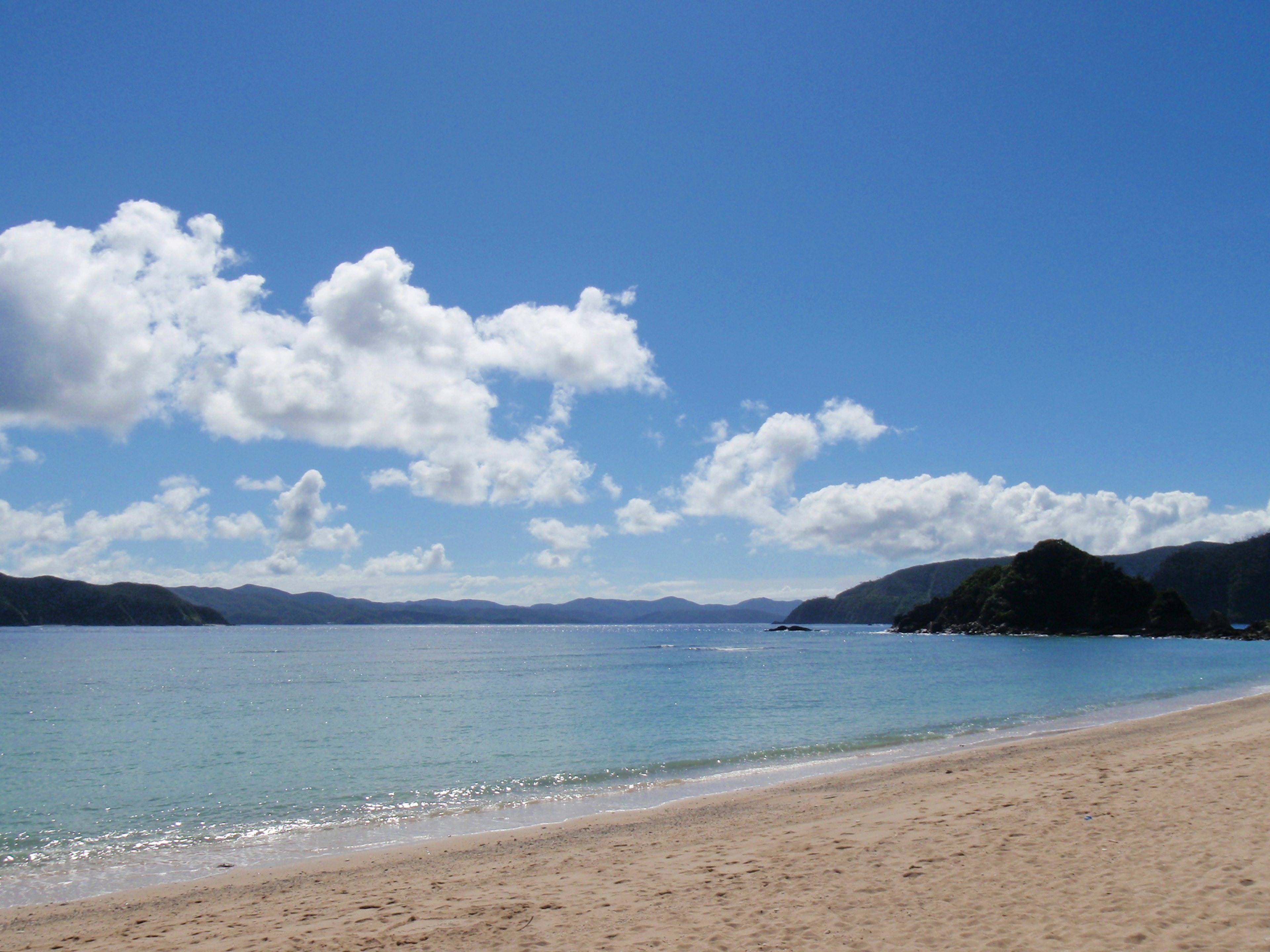 Pemandangan pantai tenang dengan langit biru dan awan putih