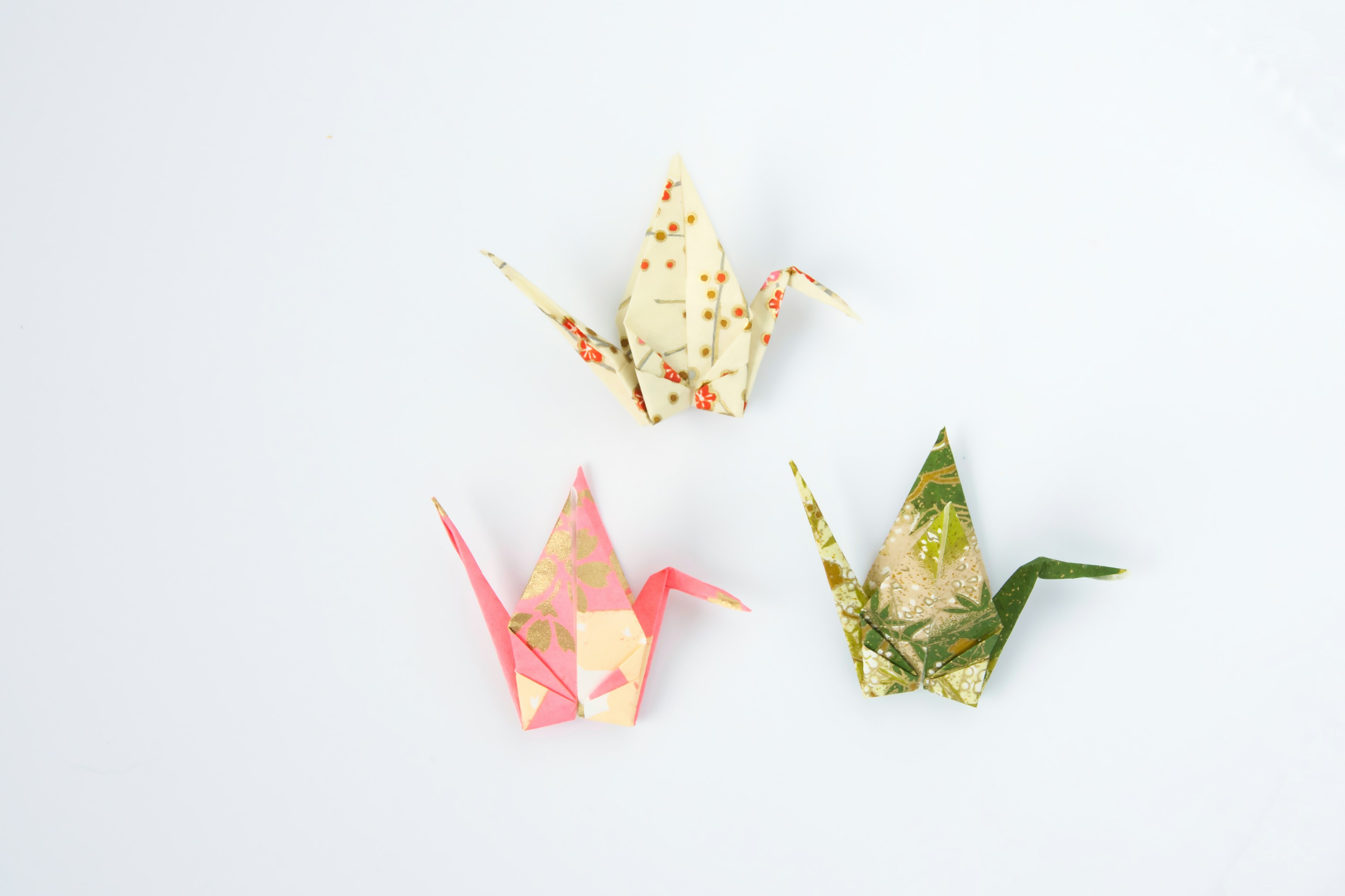 Three origami cranes in different colors and patterns arranged on a white background