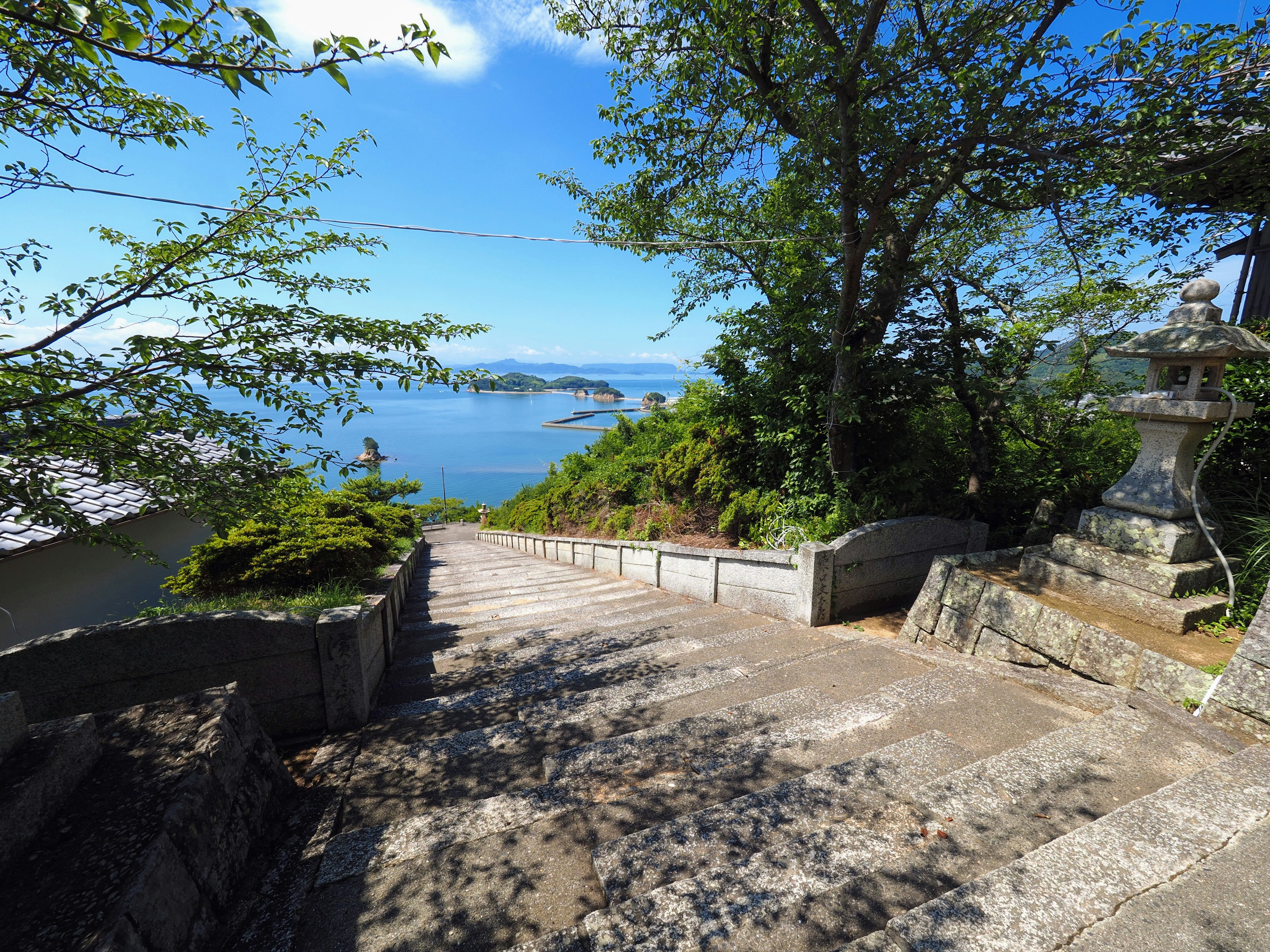 Escaleras de piedra que descienden hacia un mar azul bajo un cielo despejado con vegetación exuberante